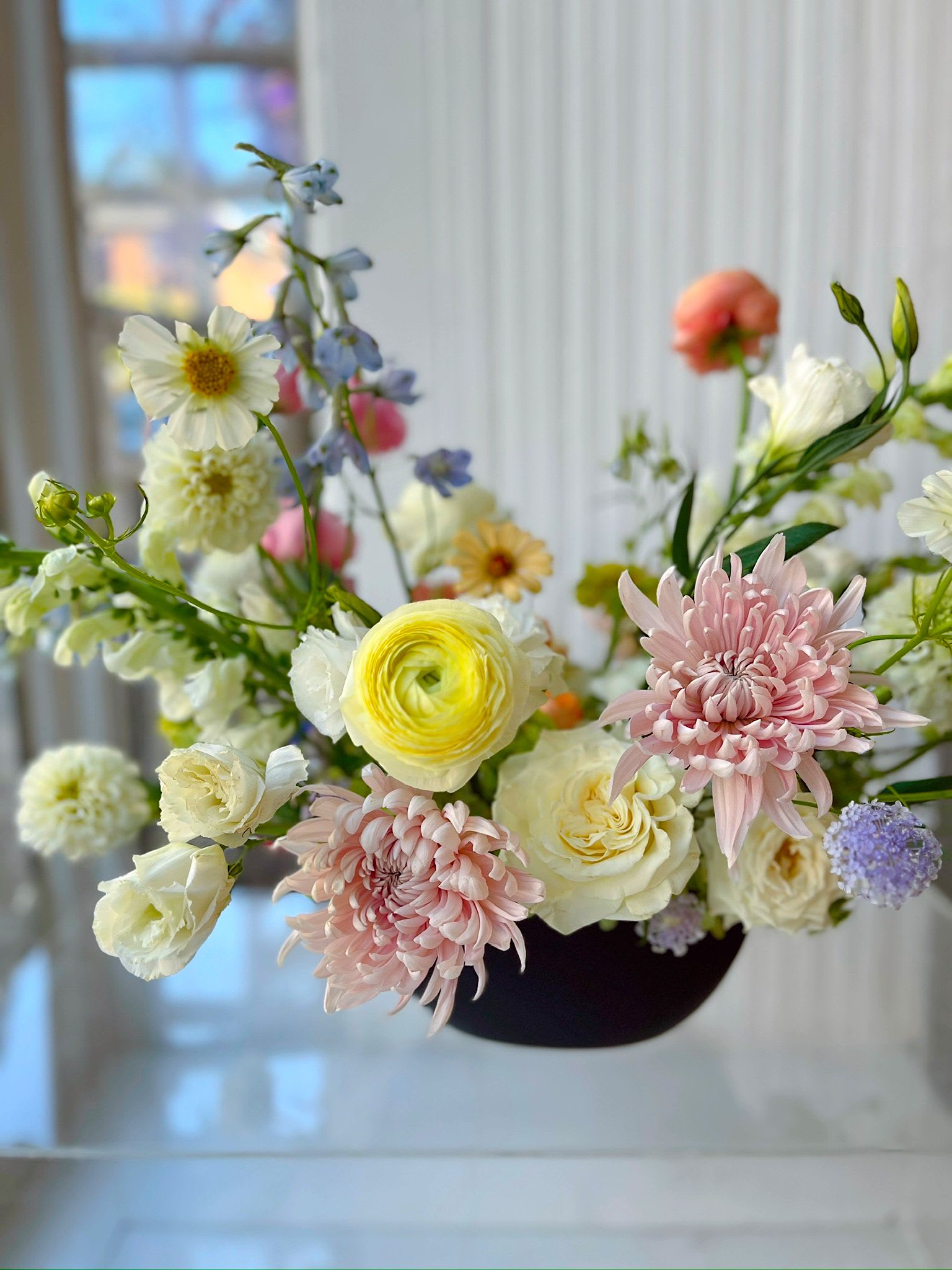 Pastel Pop - An airy, garden-inspired floral arrangement featuring blush chrysanthemums, creamy roses, ranunculus, and delicate seasonal blooms in soft pastel tones. Designed in a modern low vessel with natural movement and balance, this composition brings a light, artistic feel—perfect for home styling, thoughtful gifting, or spring occasions. Available for flower delivery in Hoboken, Jersey City, and surrounding areas.