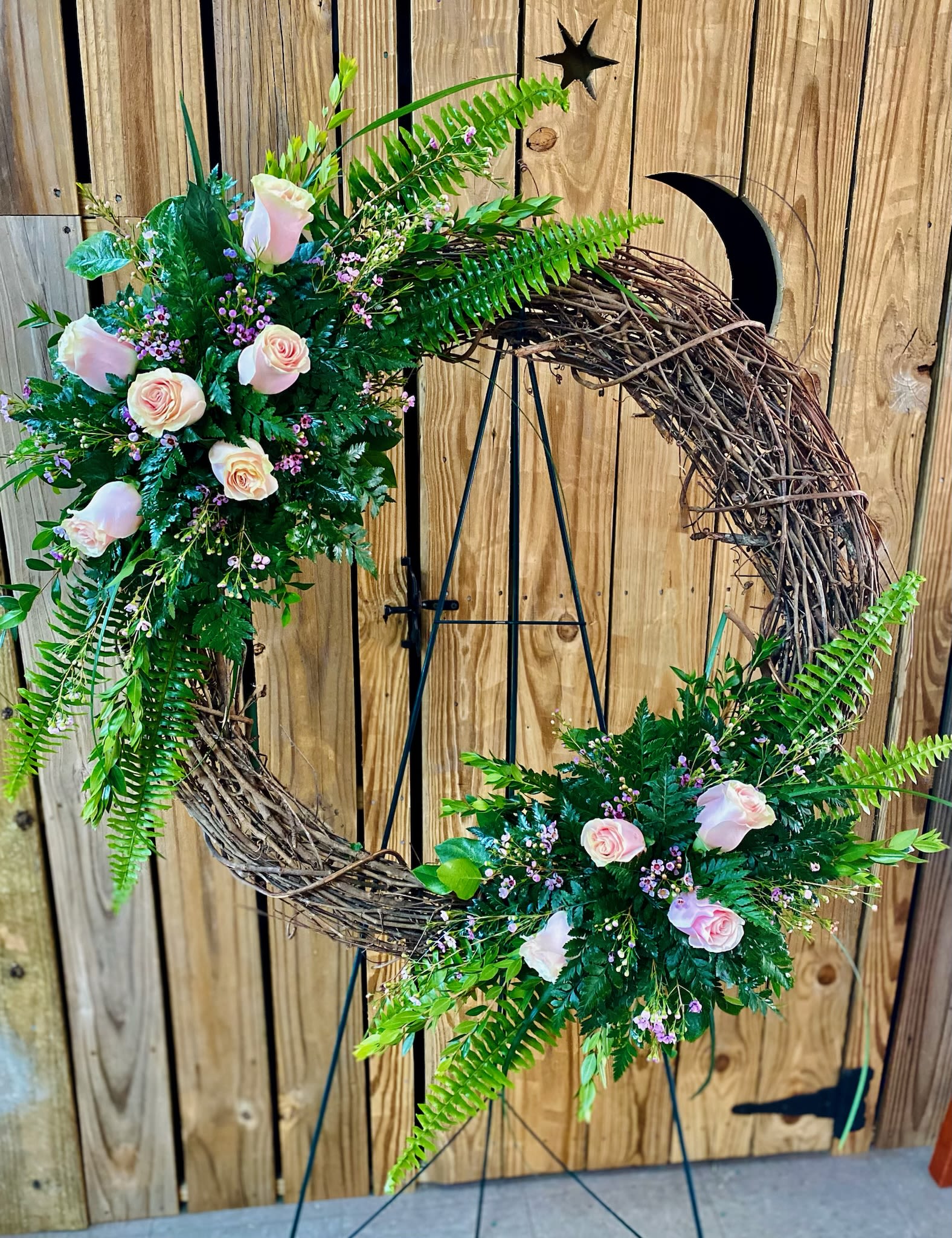 Floral crescent wreath with pale pink roses and greenery on a stand
