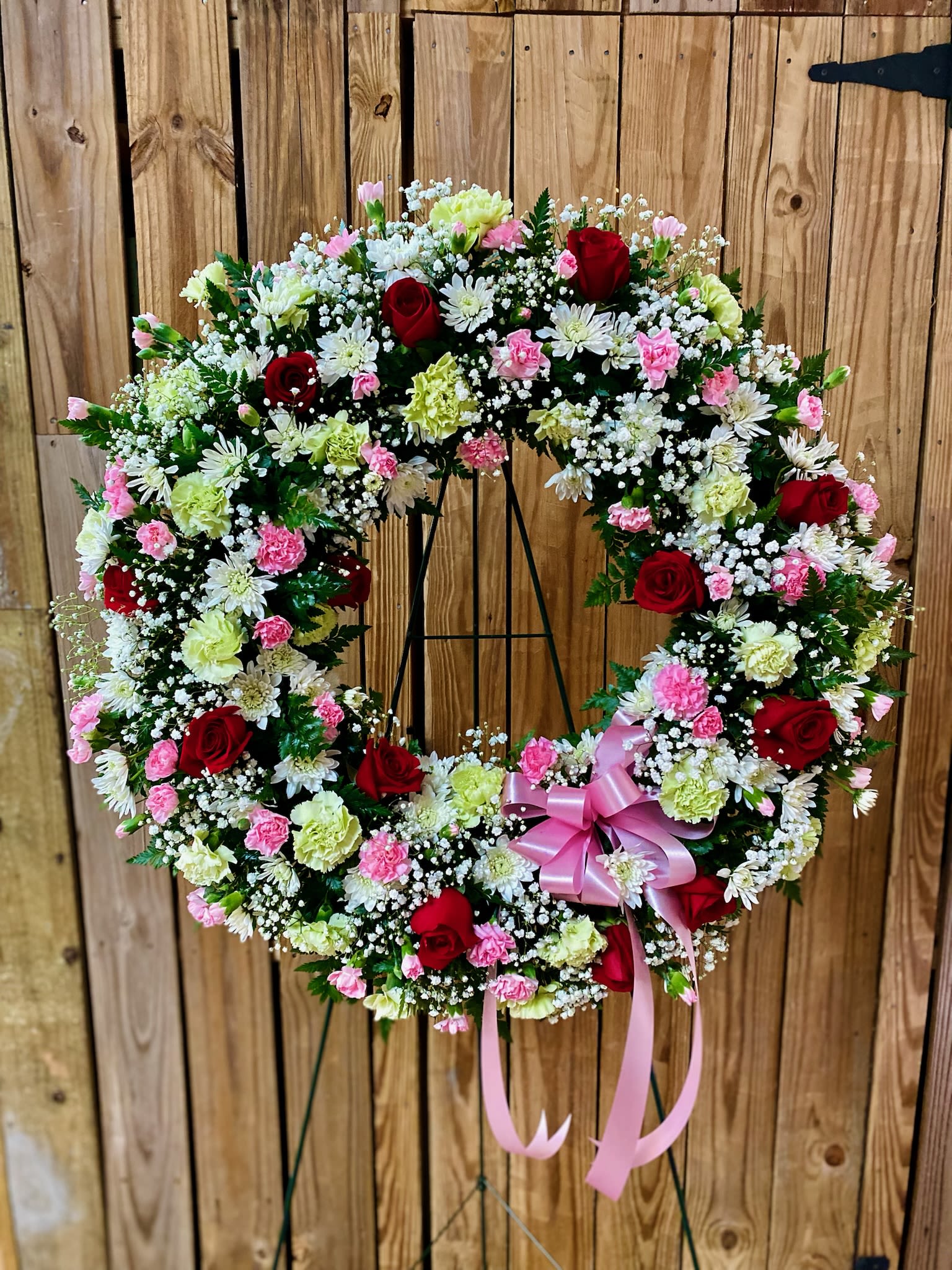 Circular floral wreath with red roses, pink carnations, and white daisies