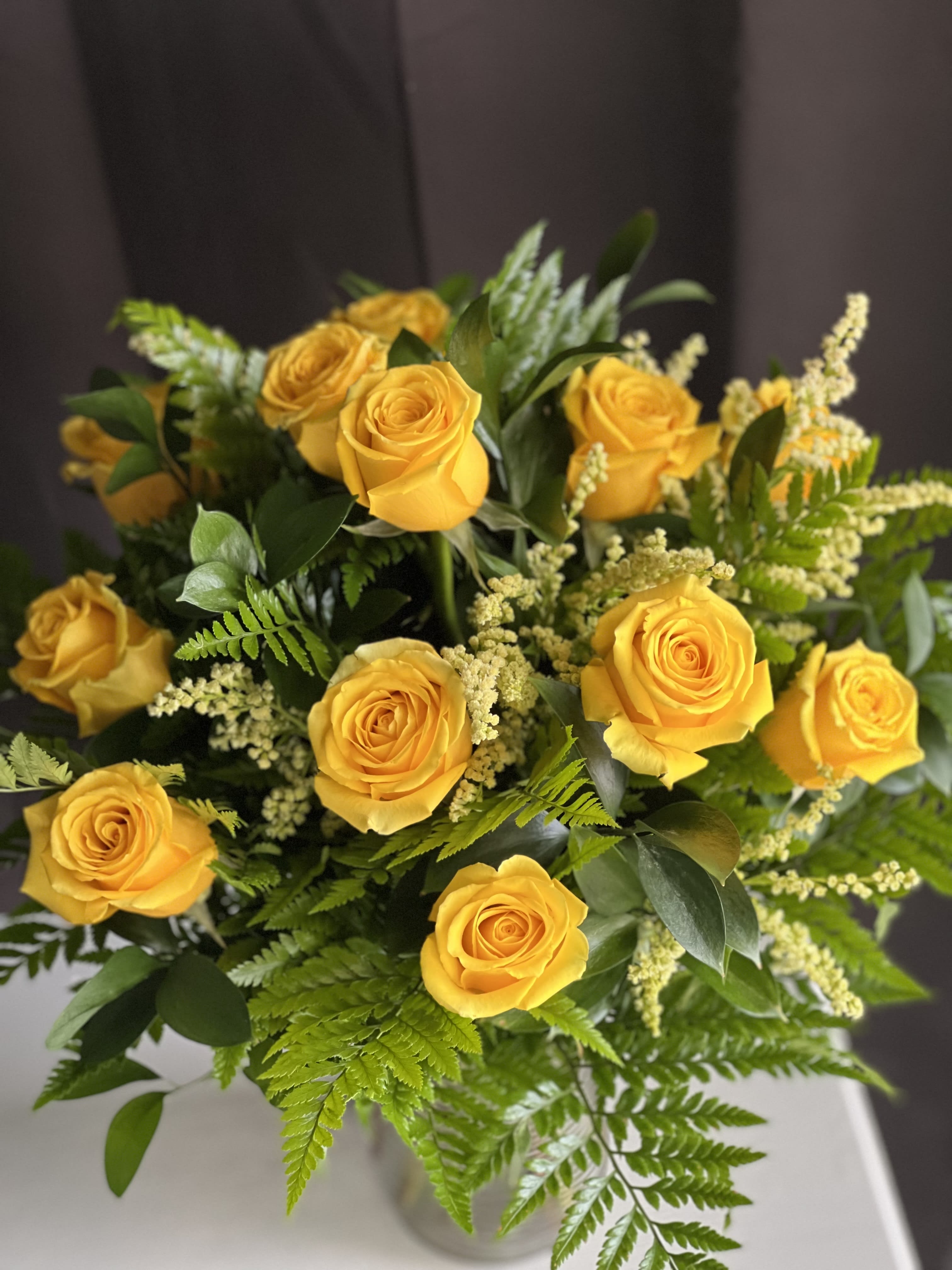 Bouquet of yellow roses with green foliage in a clear vase