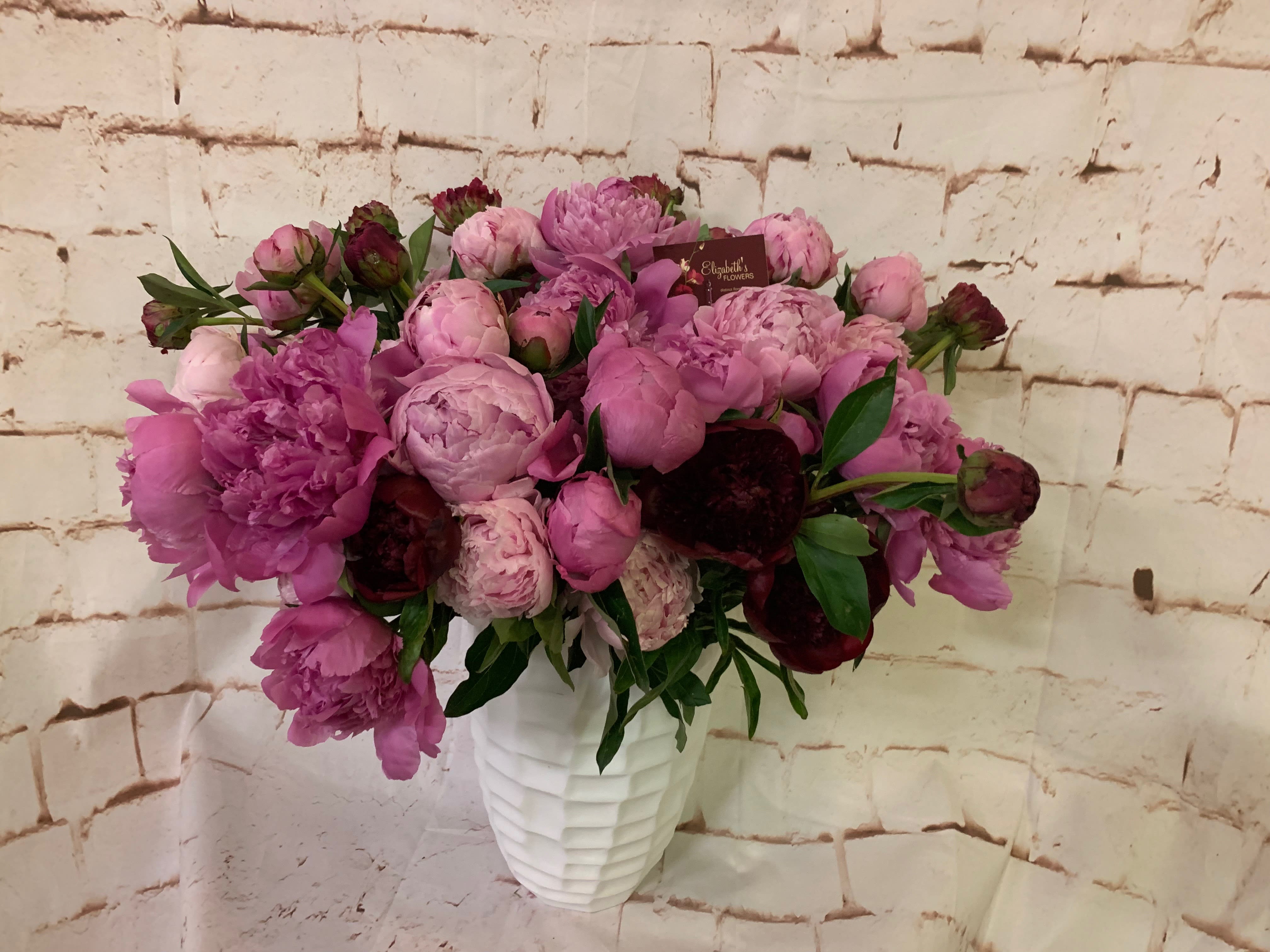 Lush arrangement of pink and burgundy peonies in a textured white vase
