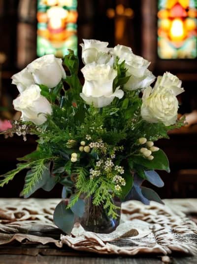 White roses arranged in a glass vase with greenery