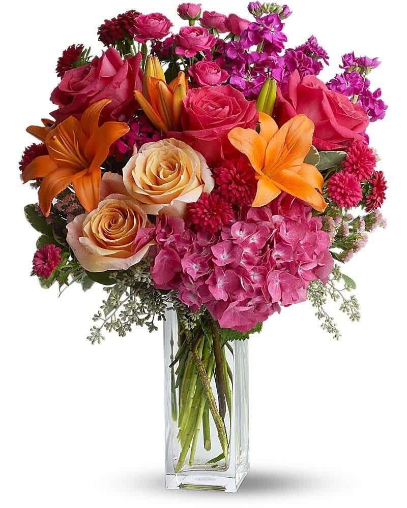 Tall arrangement of pink roses, orange lilies, and mixed pink blooms in a clear rectangular vase