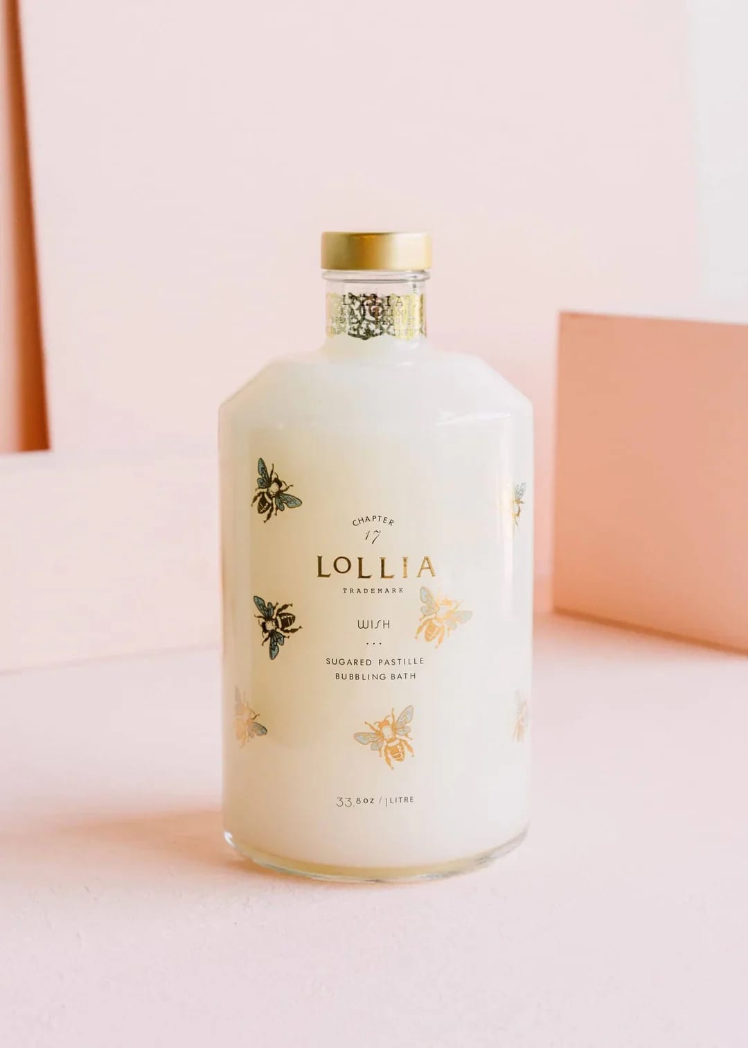 White bottle of Lollia bath product with gold cap and bee illustrations