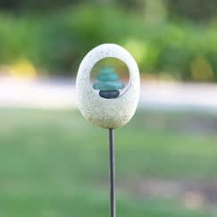 Small stone garden ornament on a metal stake with stacked blue pebbles