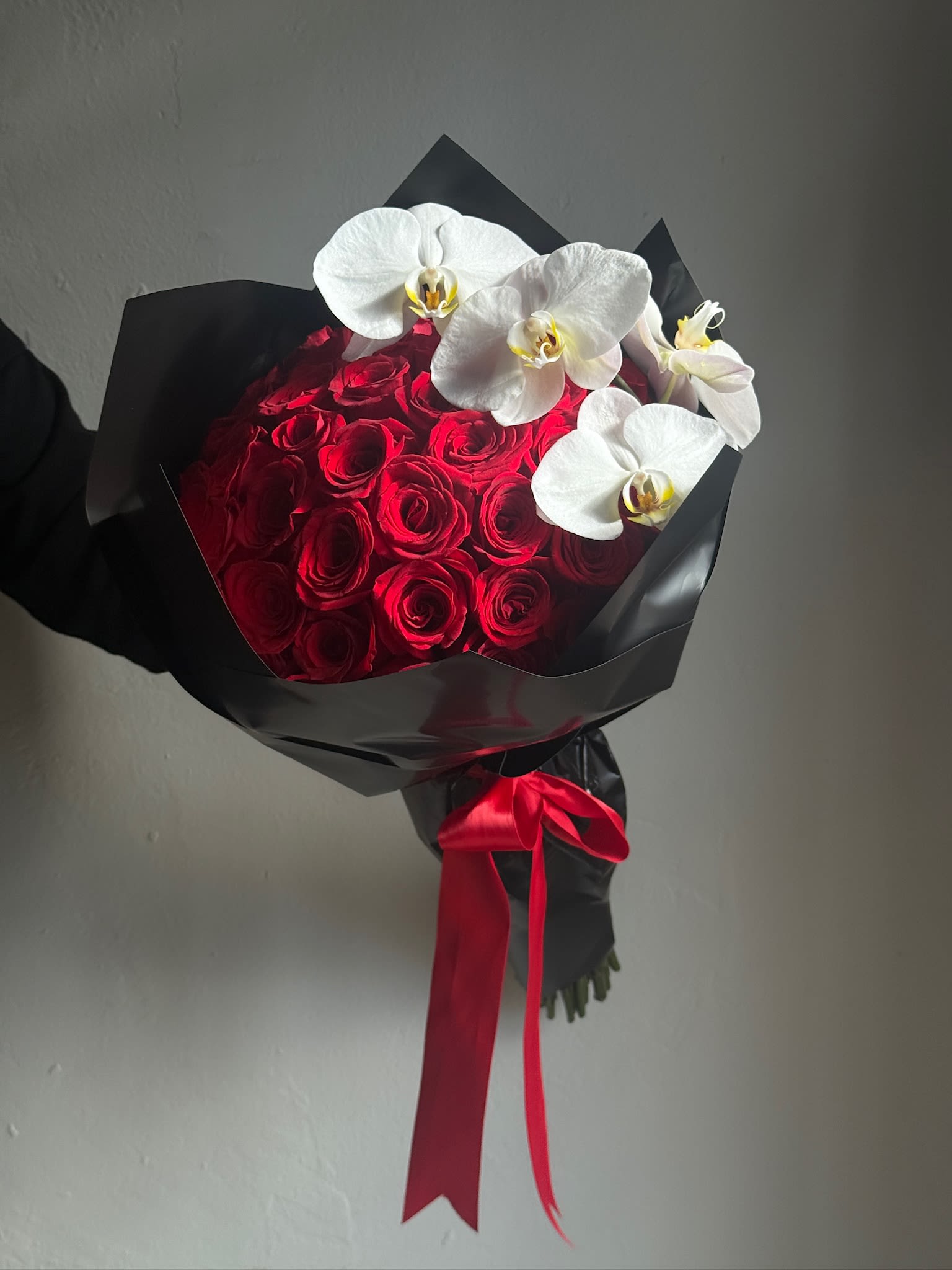 Red rose bouquet with white orchids wrapped in black paper and a red ribbon
