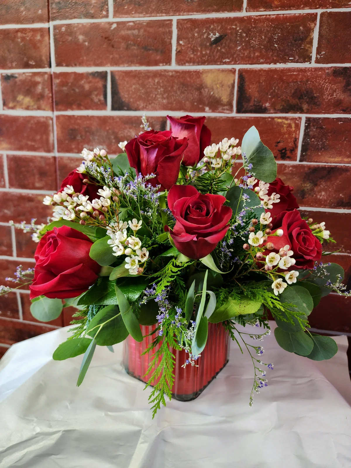 Red roses arranged in a glass vase with white filler flowers