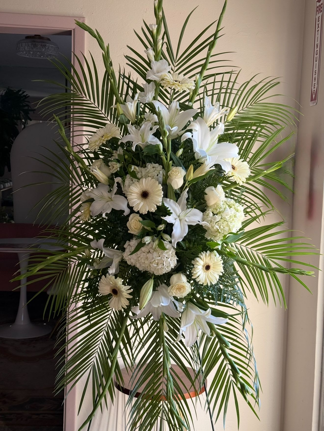 White funeral spray with lilies, gerberas, and palm fronds