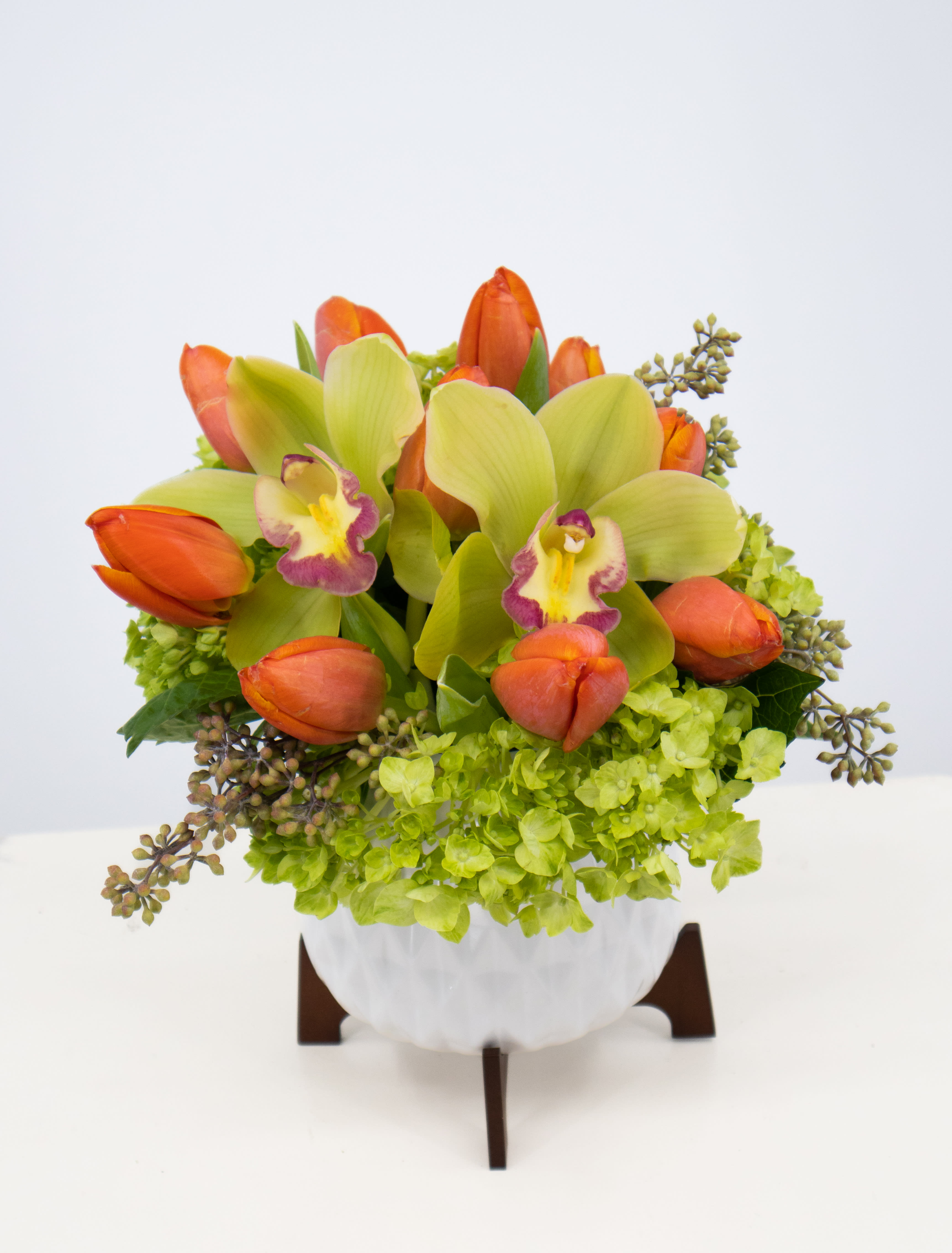 Orange tulips and green orchids in a white vase