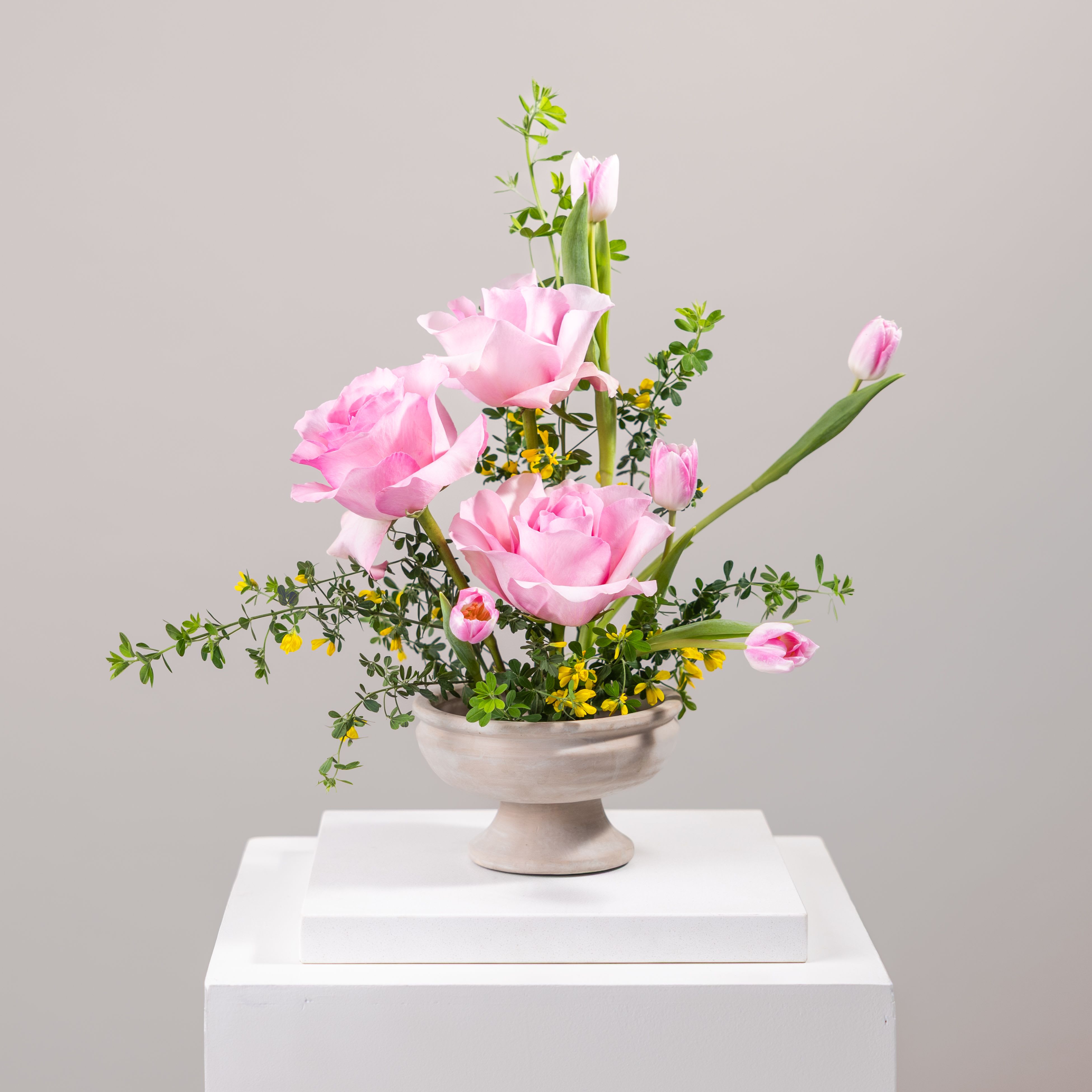 Pink tulips arranged in a pedestal vase with small yellow accents