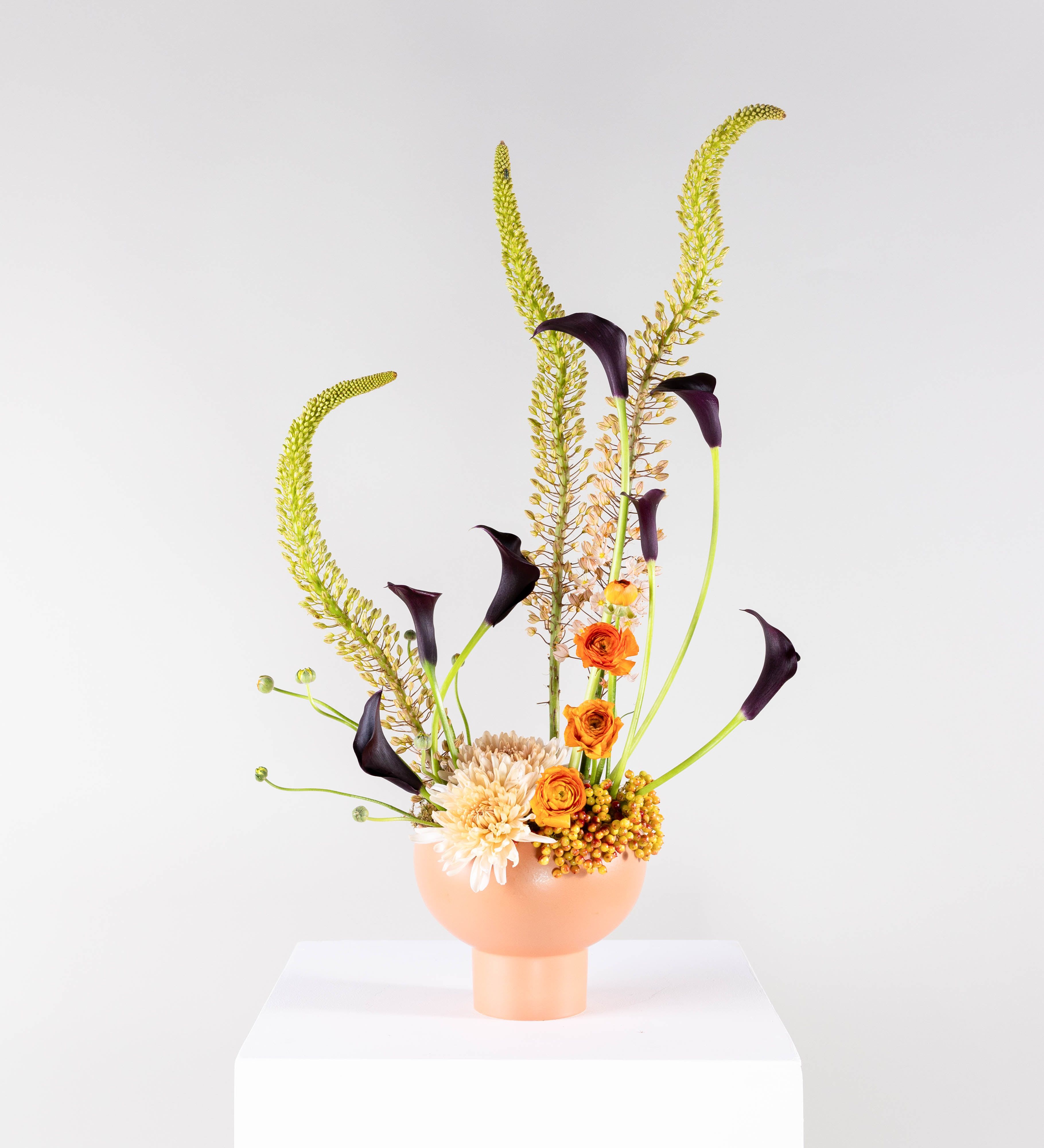 Tall floral arrangement with orange blooms and dark calla lilies in a peach vase