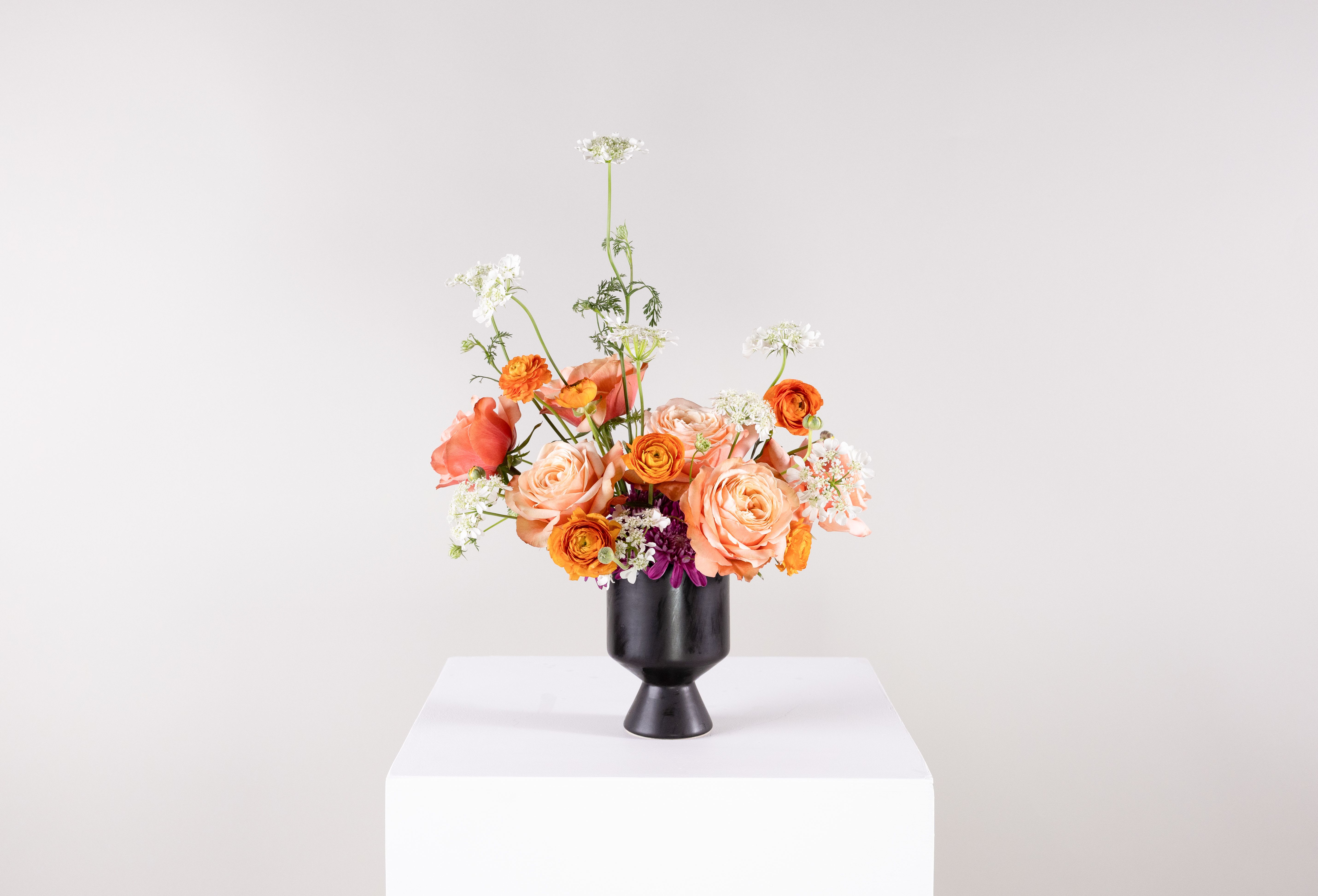 Peach and orange flower arrangement in a black vase