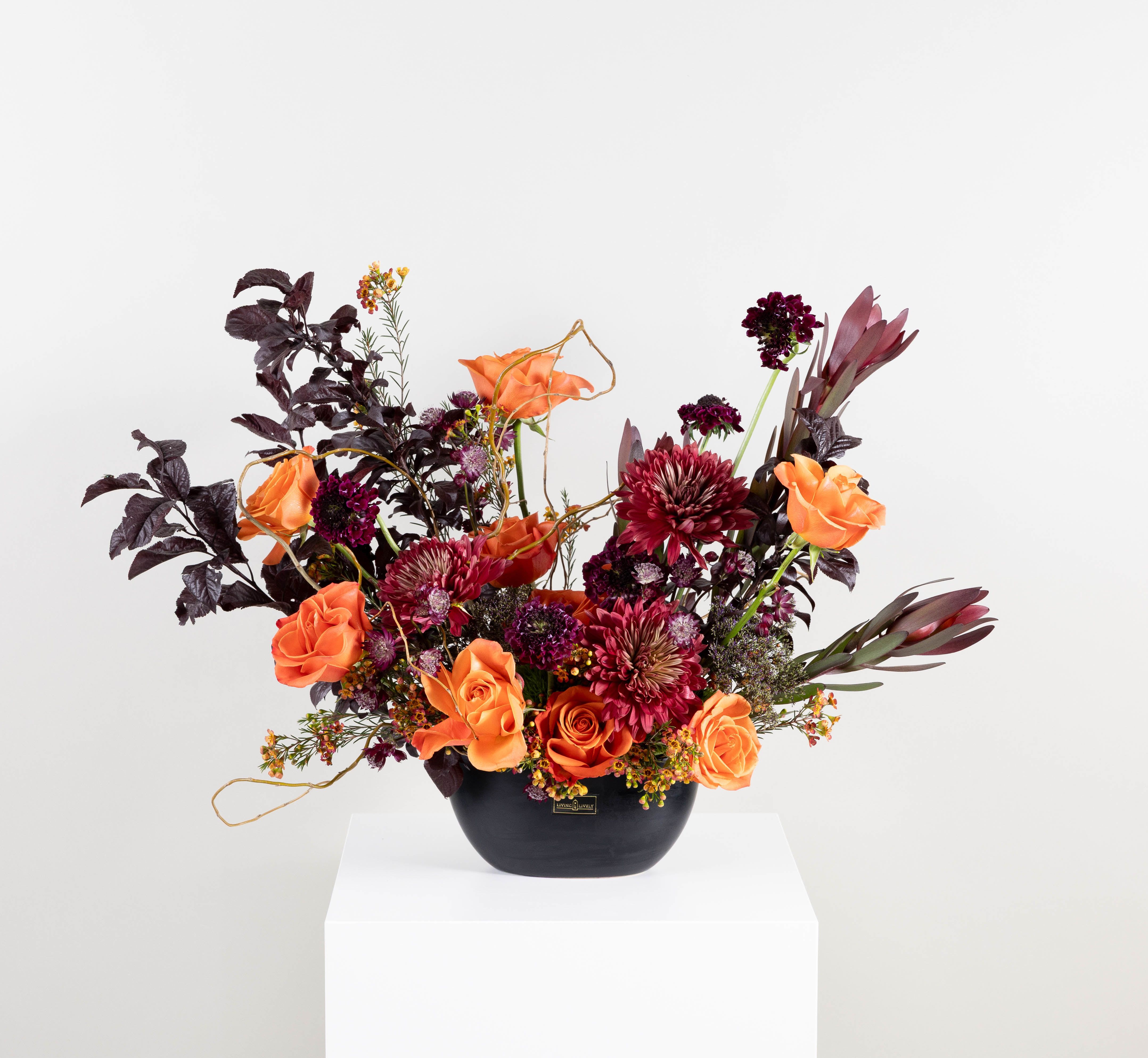 Orange roses and burgundy flowers in a black vase