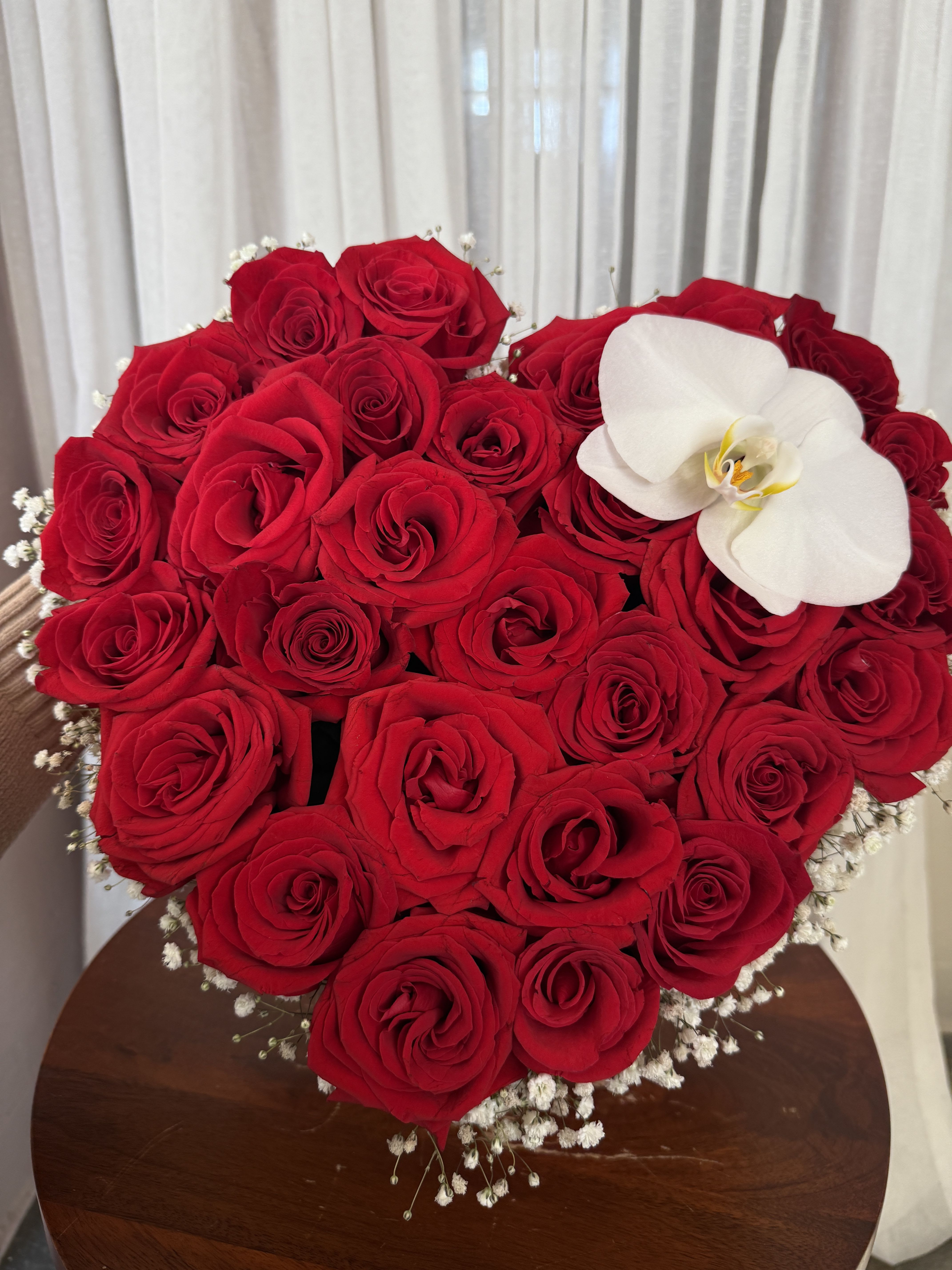 Heart-shaped bouquet of red roses with a white orchid accent