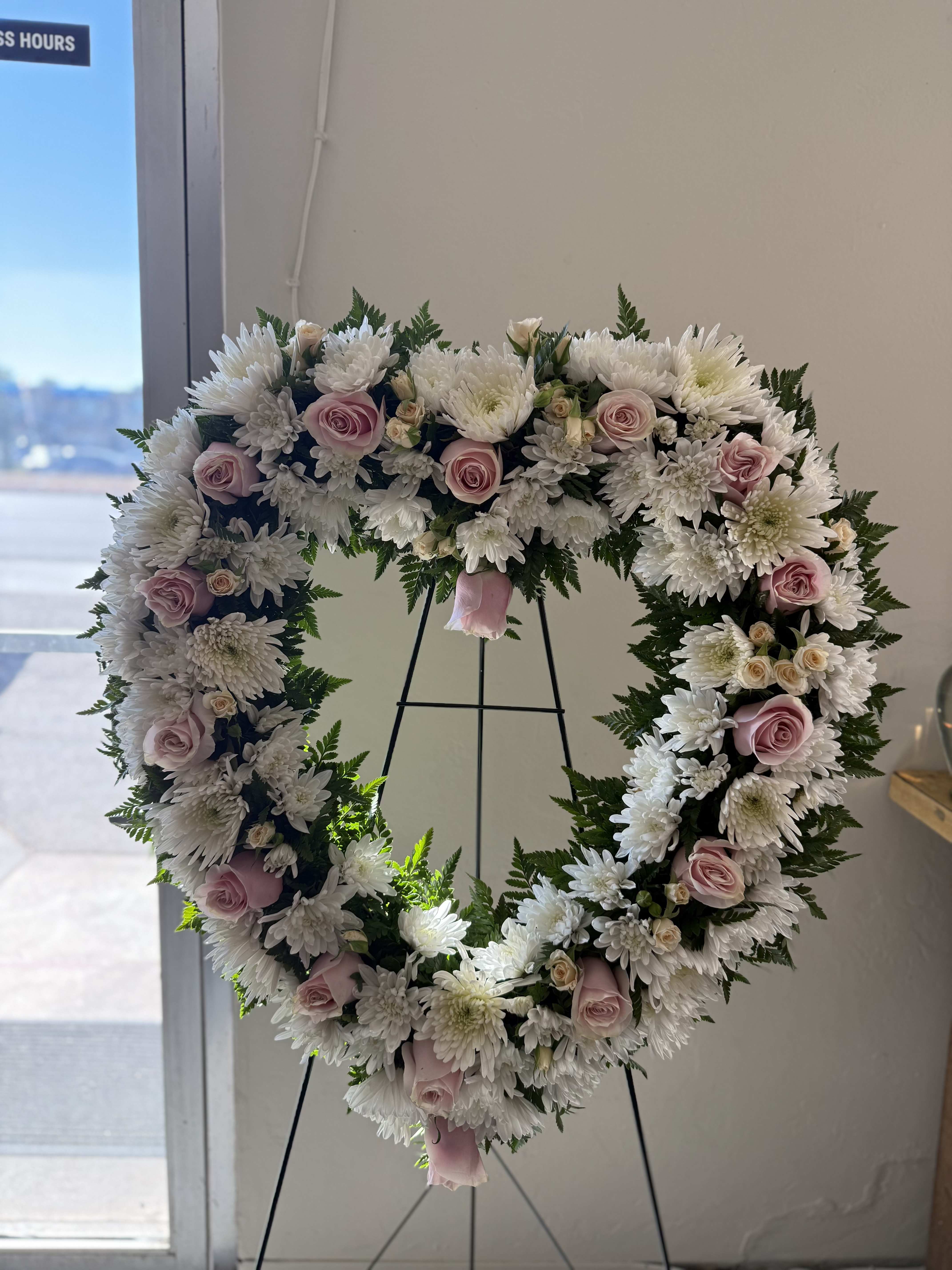 Heart-shaped standing wreath of white chrysanthemums and pale pink roses on a metal easel.