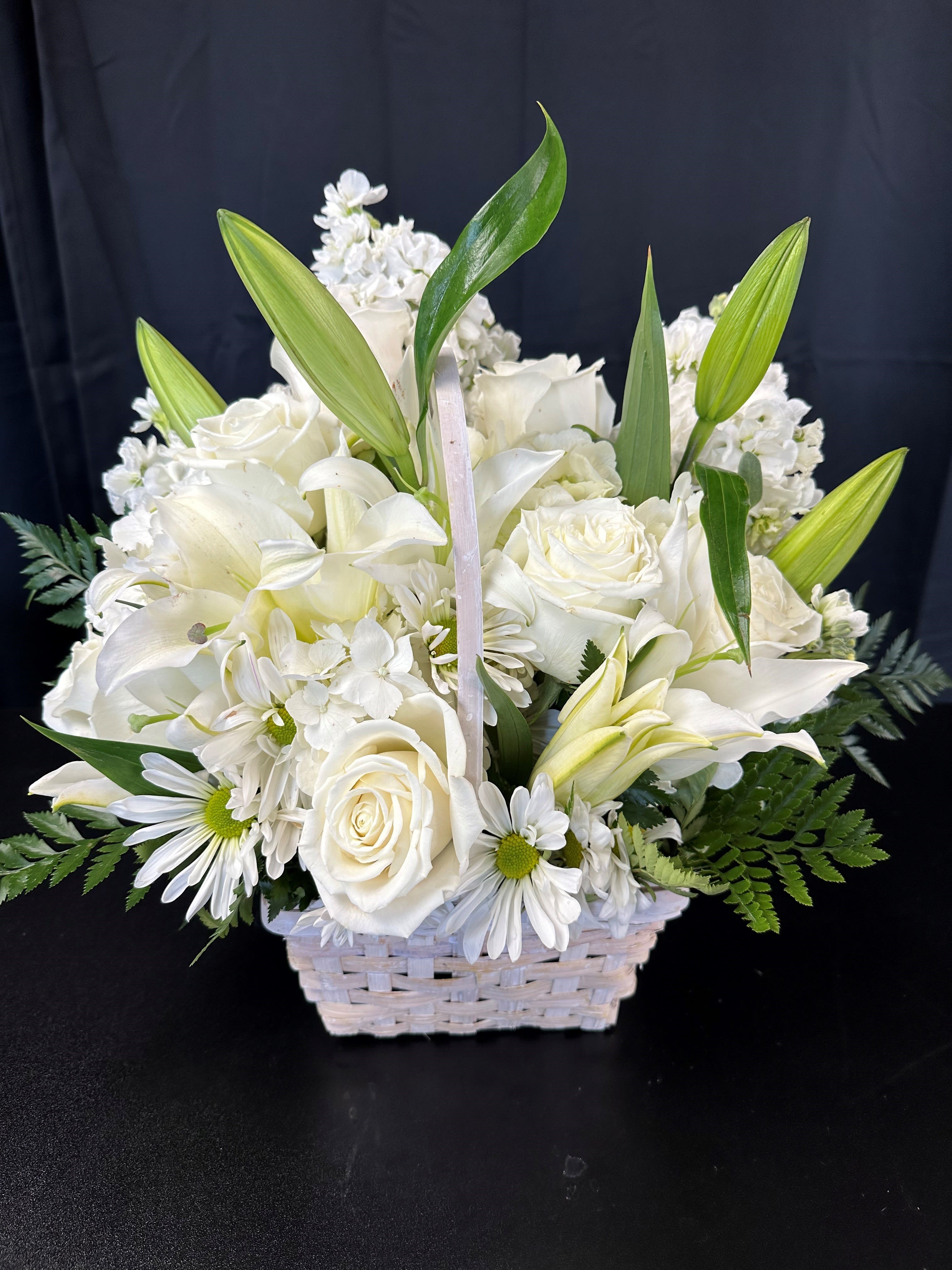 White floral arrangement in a woven basket with lilies and roses