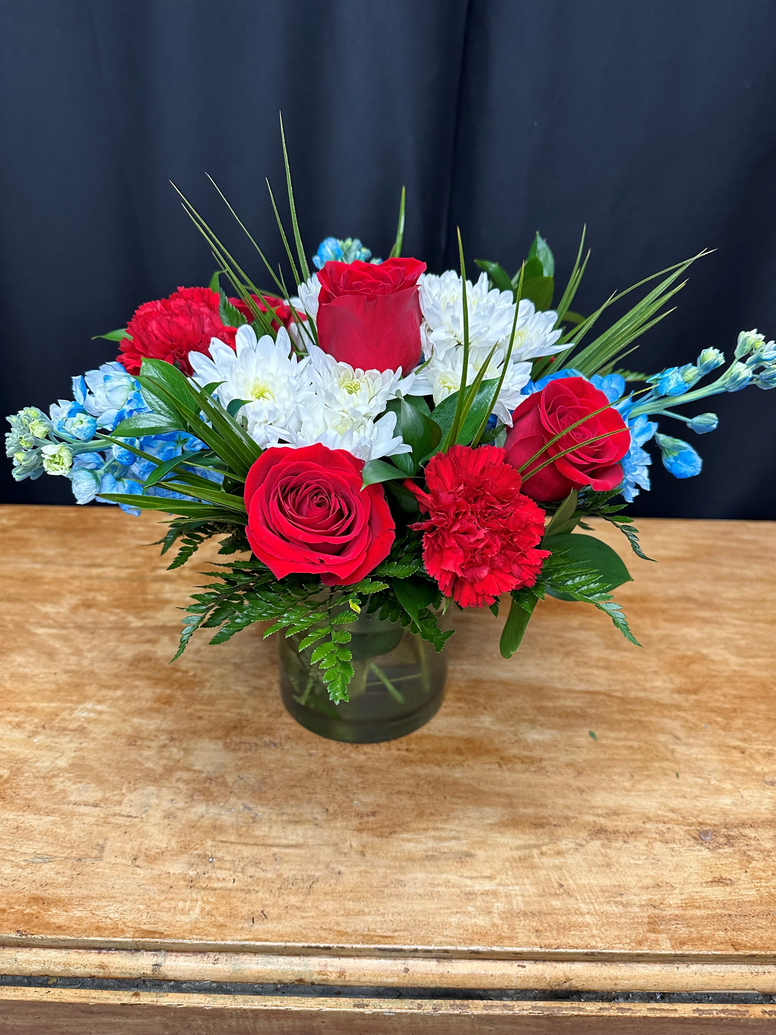Red roses and white daisies in a glass vase with blue accents