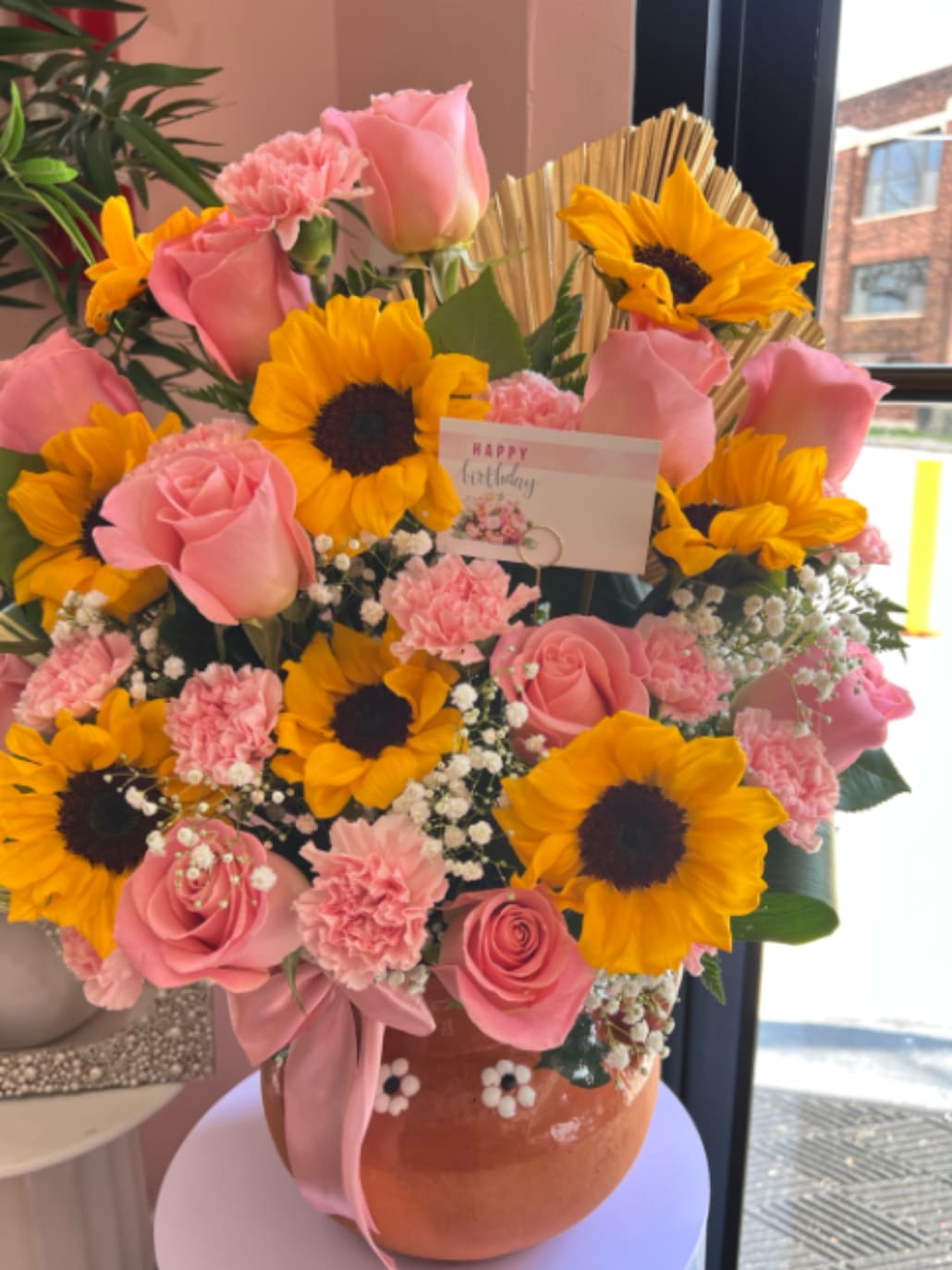 Amorsito Corazon - This beautiful floral arrangement combines the warmth and joy of sunflowers with the delicacy of pink roses and the charming texture of pink carnations, creating a harmonious and vibrant composition. It is designed in a traditional Mexican clay pot (cantarito), adding an artisanal, authentic, and very special touch 