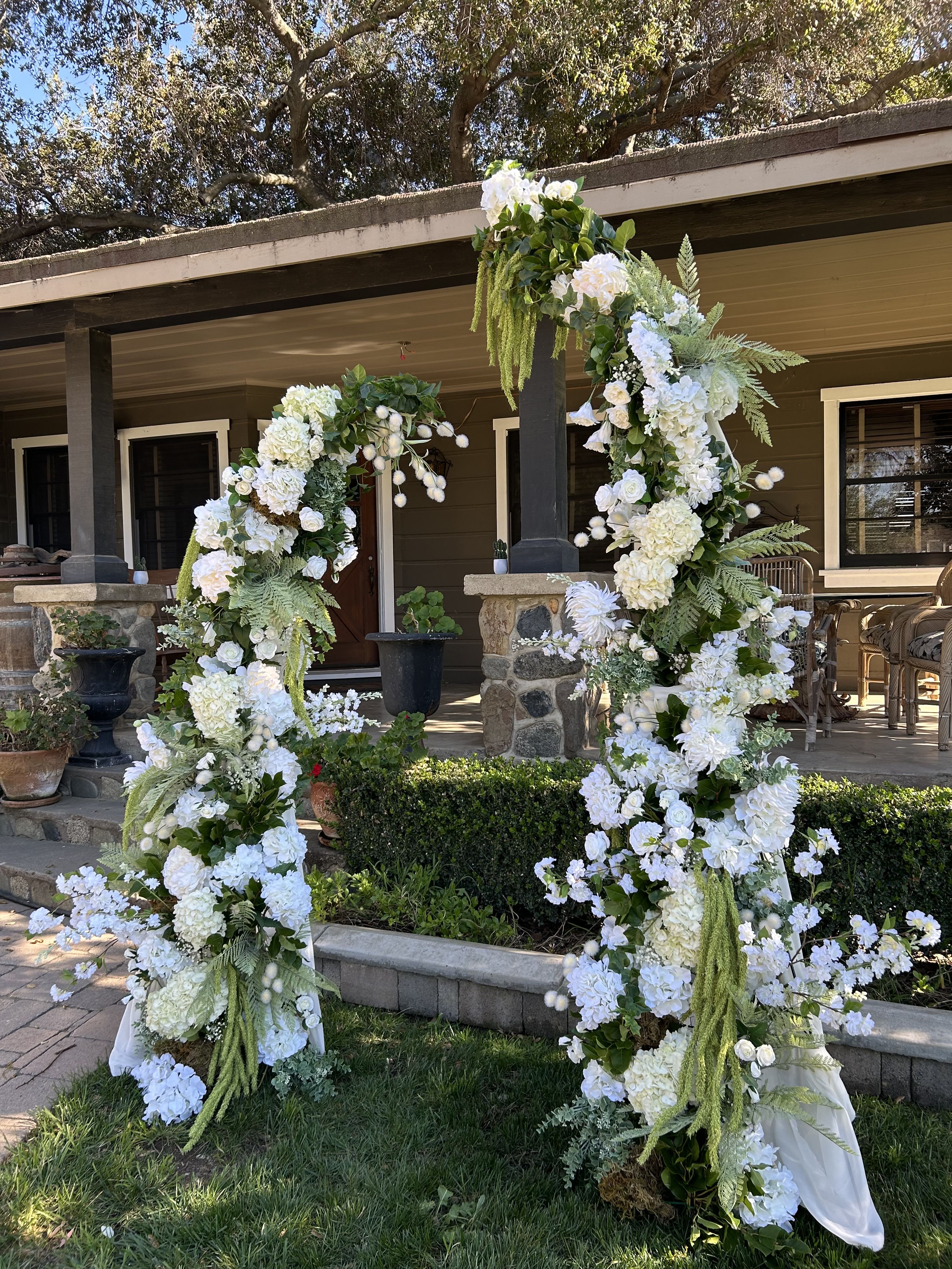 Event Arch Rental - Create a beautiful focal point for your event with our faux floral arch rental in Orange County. Designed with a lush base of premium real-feel faux florals, this arch provides a full, romantic backdrop that photographs beautifully for weddings, bridal showers, baby showers, corporate events, and special celebrations.  Tall arch measures at 8ft  What makes our arch unique is the natural, enhanced design. The base is built with high-quality faux flowers to create a full and consistent foundation, while fresh greenery and seasonal real flowers are added to bring texture, movement, and a lifelike appearance. This combination gives you the best of both worlds — the reliability and fullness of faux florals with the natural beauty of real floral elements.  Available for events in Irvine, Newport Beach, Costa Mesa, Santa Ana, and across Orange County, this arch is a stunning and versatile statement piece that elevates any celebration while creating an unforgettable photo backdrop for your guests