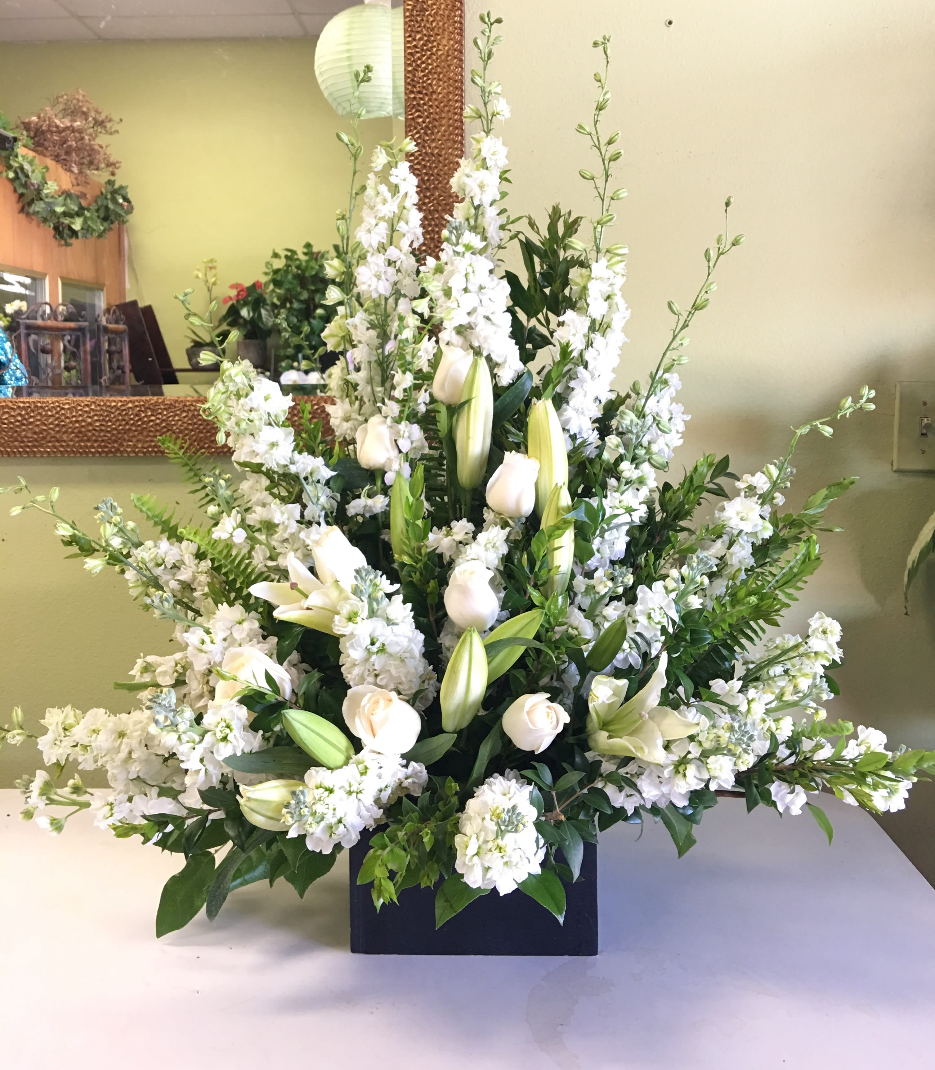 Large white floral arrangement with lilies and roses in a black container