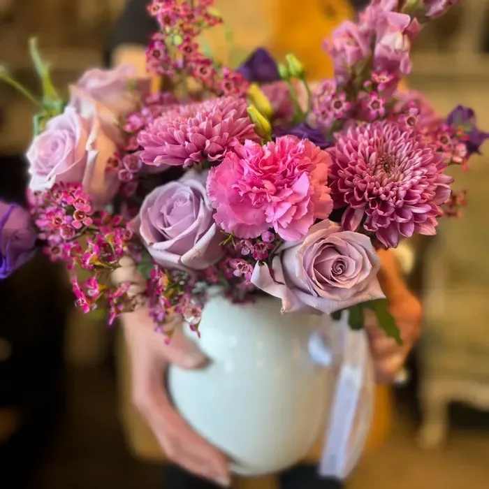 The Martha: Pitcher with Blooms - Make Mother’s Day unforgettable with The Martha—a stunning, hand-arranged seasonal bouquet designed to delight. Choose from soft pinks, rich purples, or vibrant mixed florals, all thoughtfully styled in a white ceramic pitcher that doubles as a keepsake. This elegant floral arrangement is crafted in our local floral studio using fresh, locally grown blooms and lots of love. A perfect blend of classic beauty and modern design, The Martha is more than just a gift—it’s a heartfelt experience. Available for Mother’s Day flower delivery from your favorite local florist.  Product ID: The-Martha 