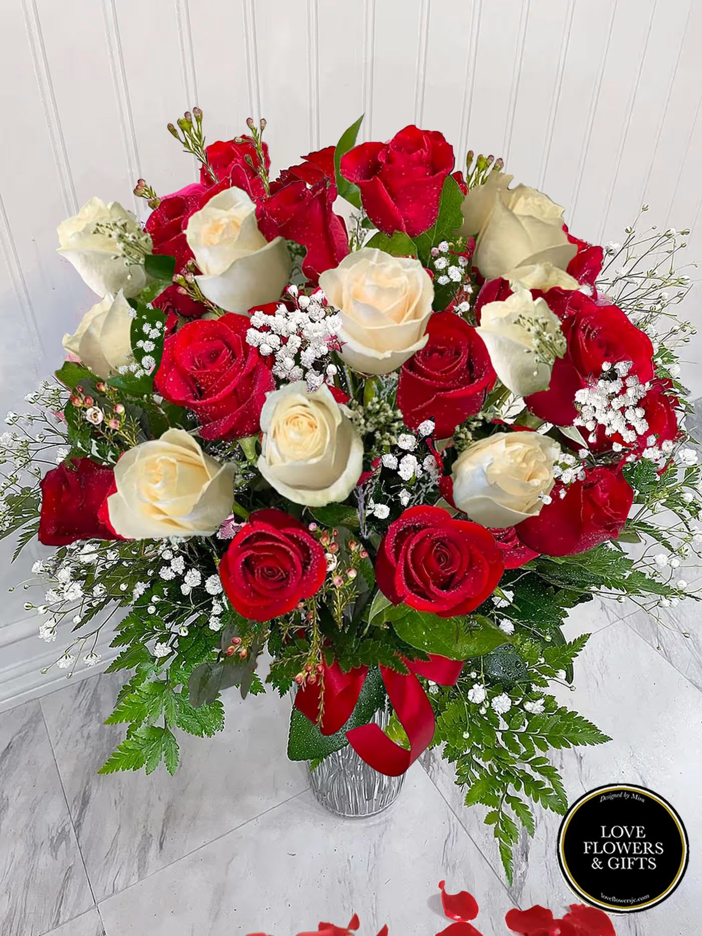 Tall vase arrangement of red and cream roses with baby's breath and a red ribbon