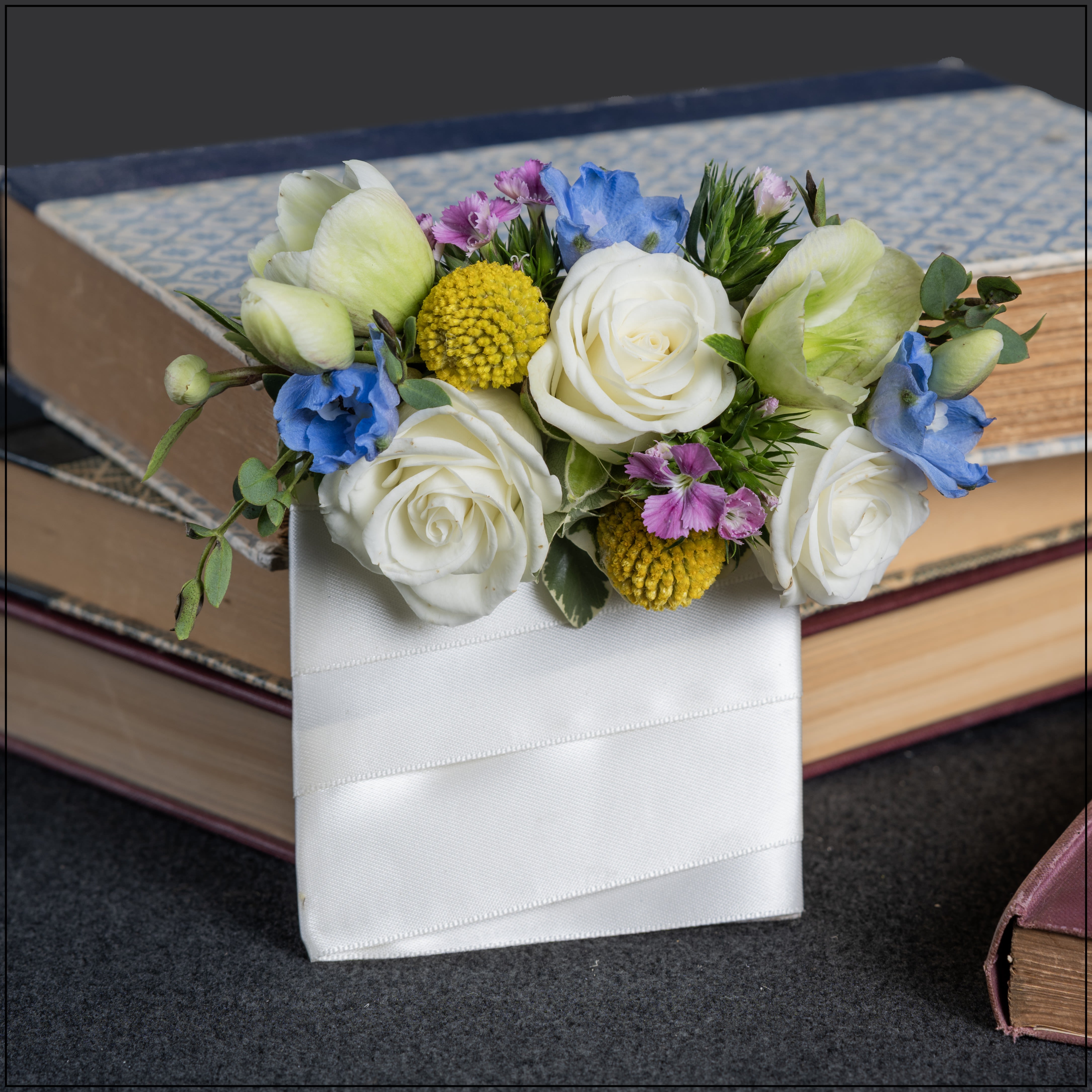 White roses and blue flowers arranged in a white ribbon-wrapped holder