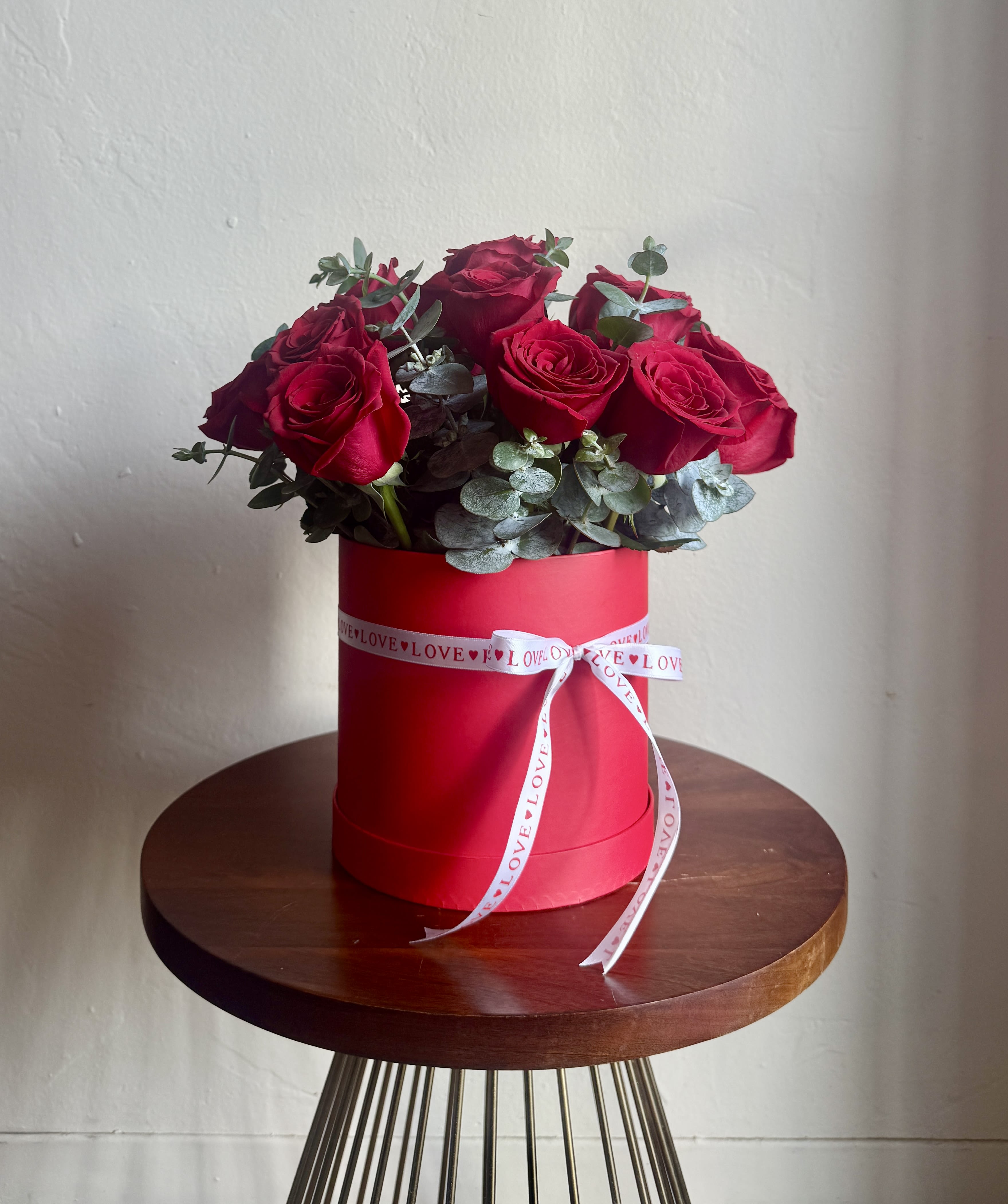 Red roses arranged in a red hat box with a white ribbon