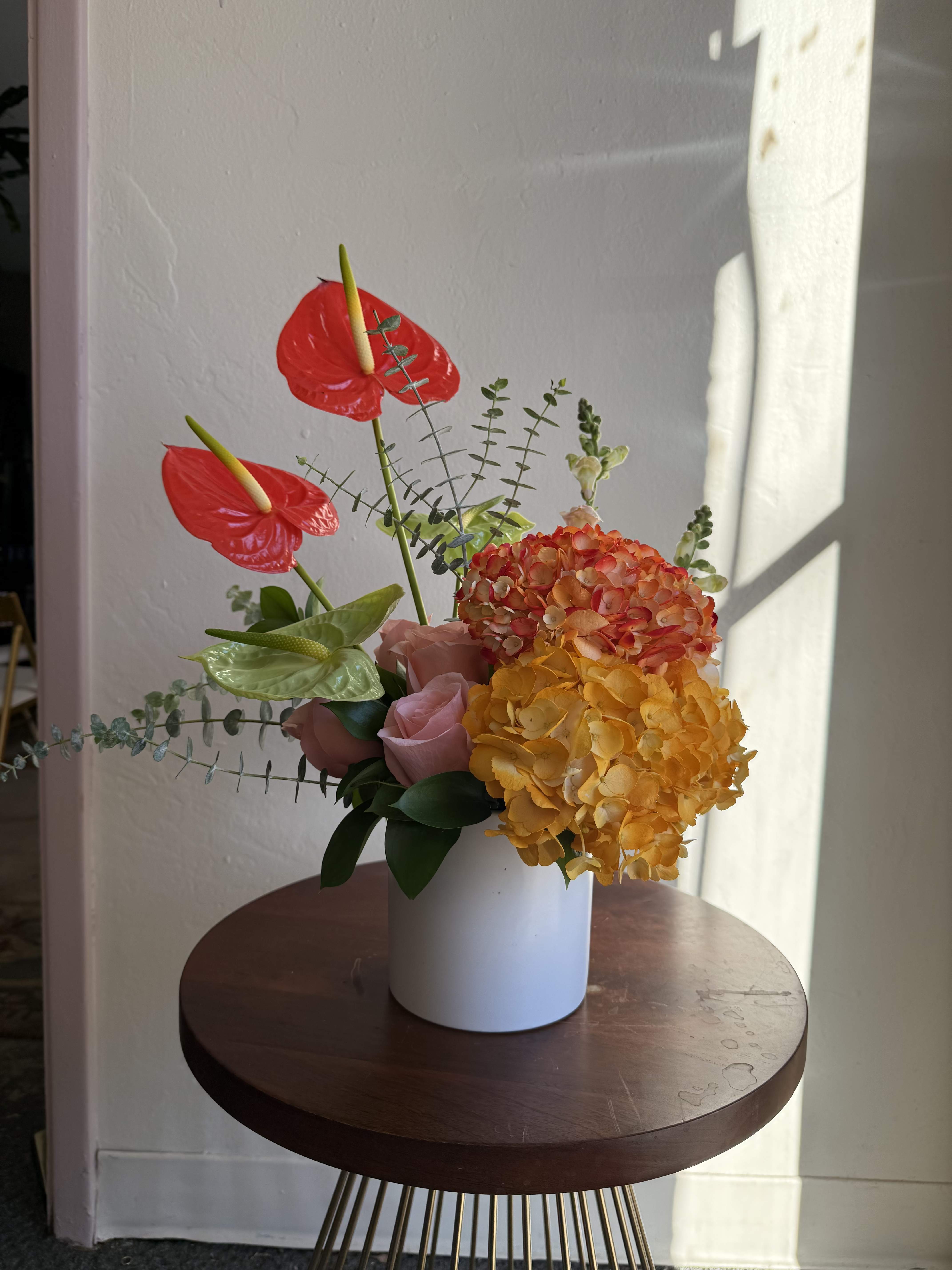 Arrangement of red anthuriums, hydrangeas, and pink roses in a white vase