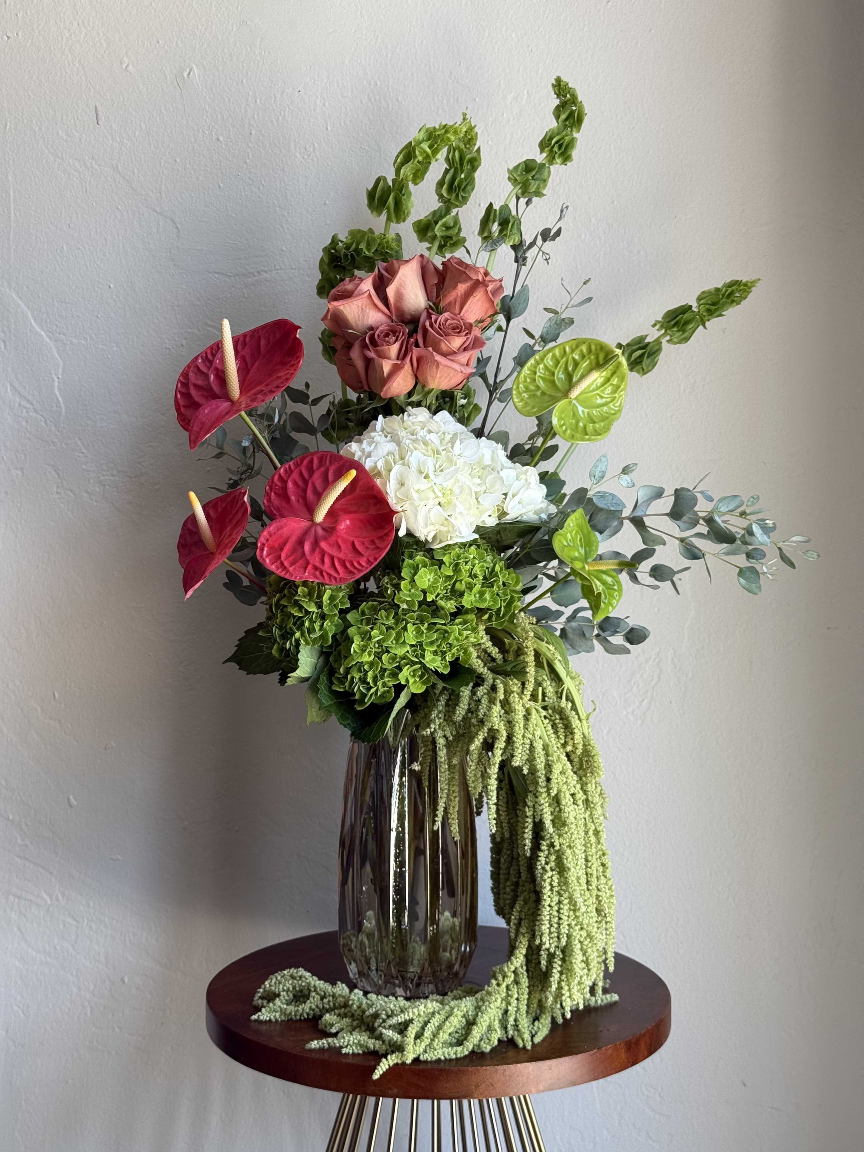 Tall floral arrangement with roses, hydrangea, and anthuriums in a glass vase