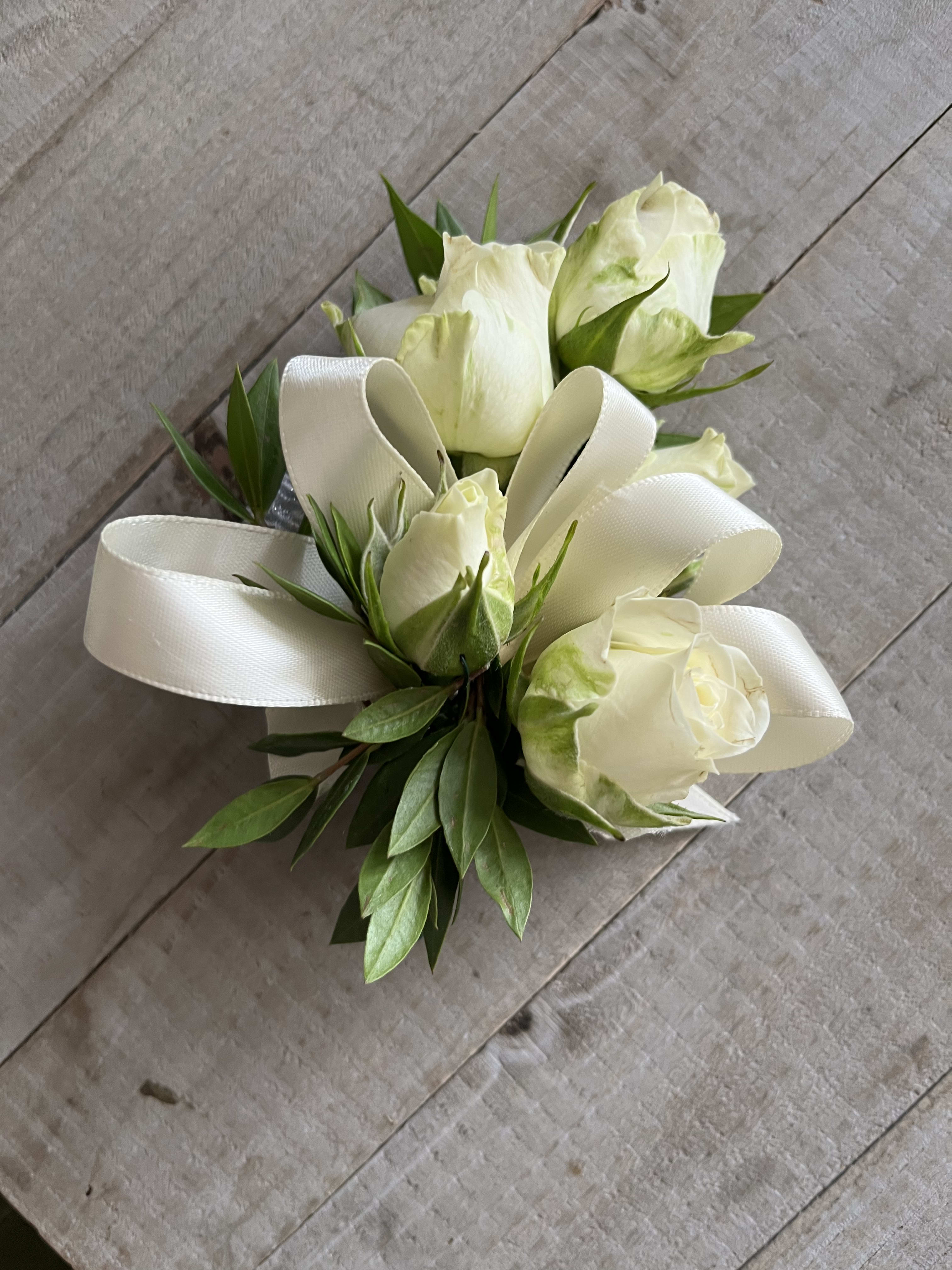 White rose boutonniere with green leaves and a white ribbon