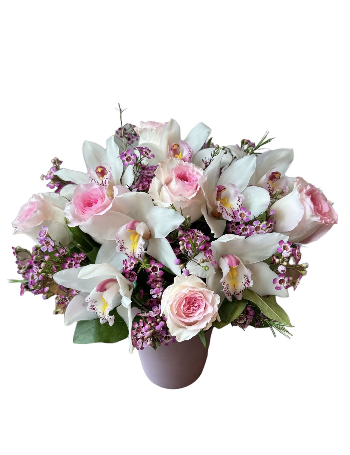 Low arrangement of pink roses, white cymbidium orchids, and tiny purple blooms in a soft pink vase
