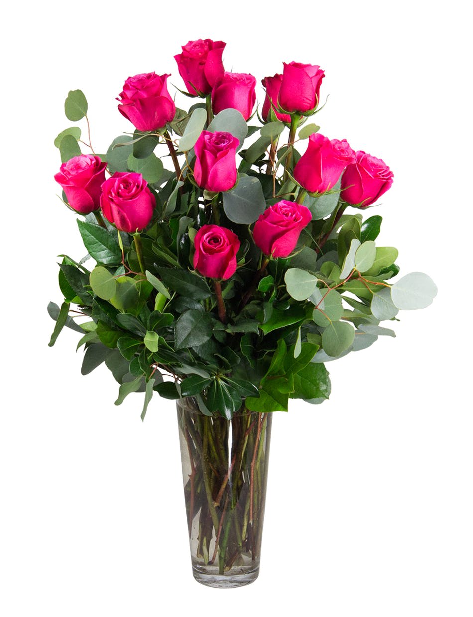 Tall arrangement of bright pink roses with lush foliage in a clear glass vase