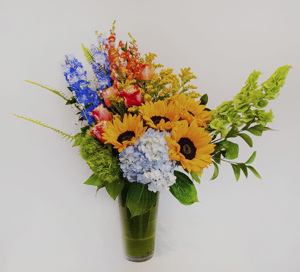 Colorful bouquet with sunflowers, hydrangea, and snapdragons in a glass vase