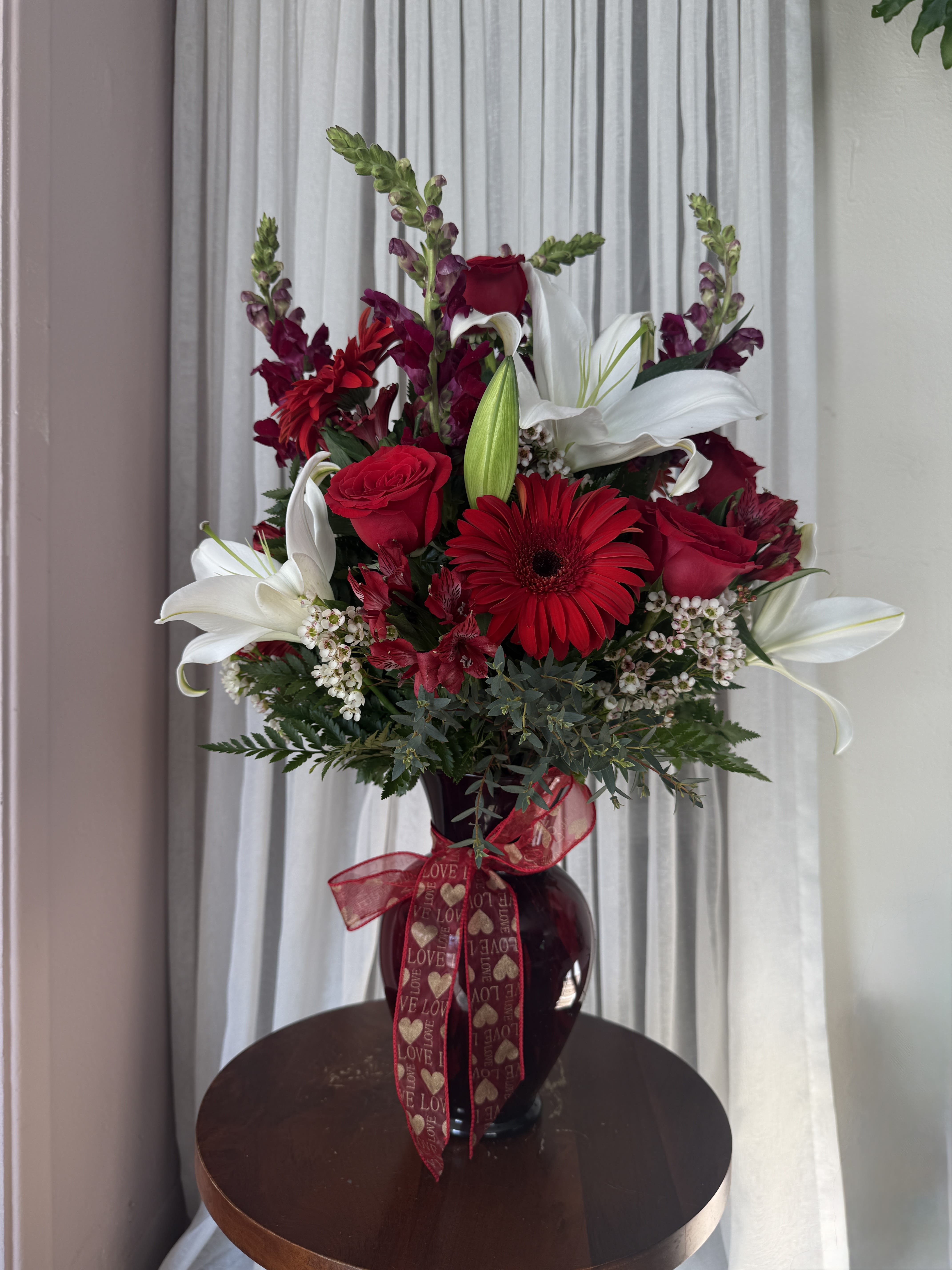 Red and white floral arrangement in a dark vase with a heart ribbon
