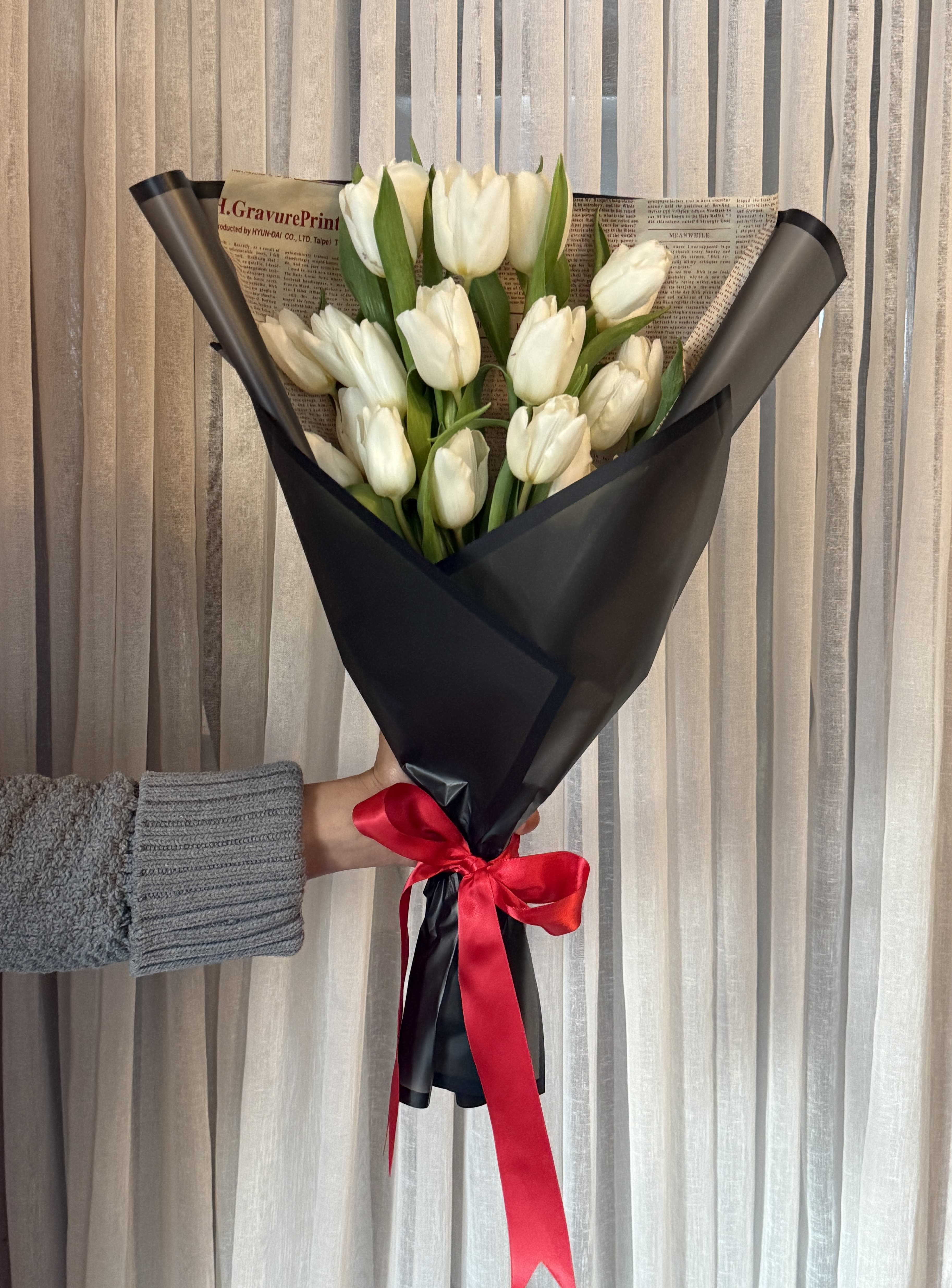 Bouquet of white tulips wrapped in black paper with a red ribbon
