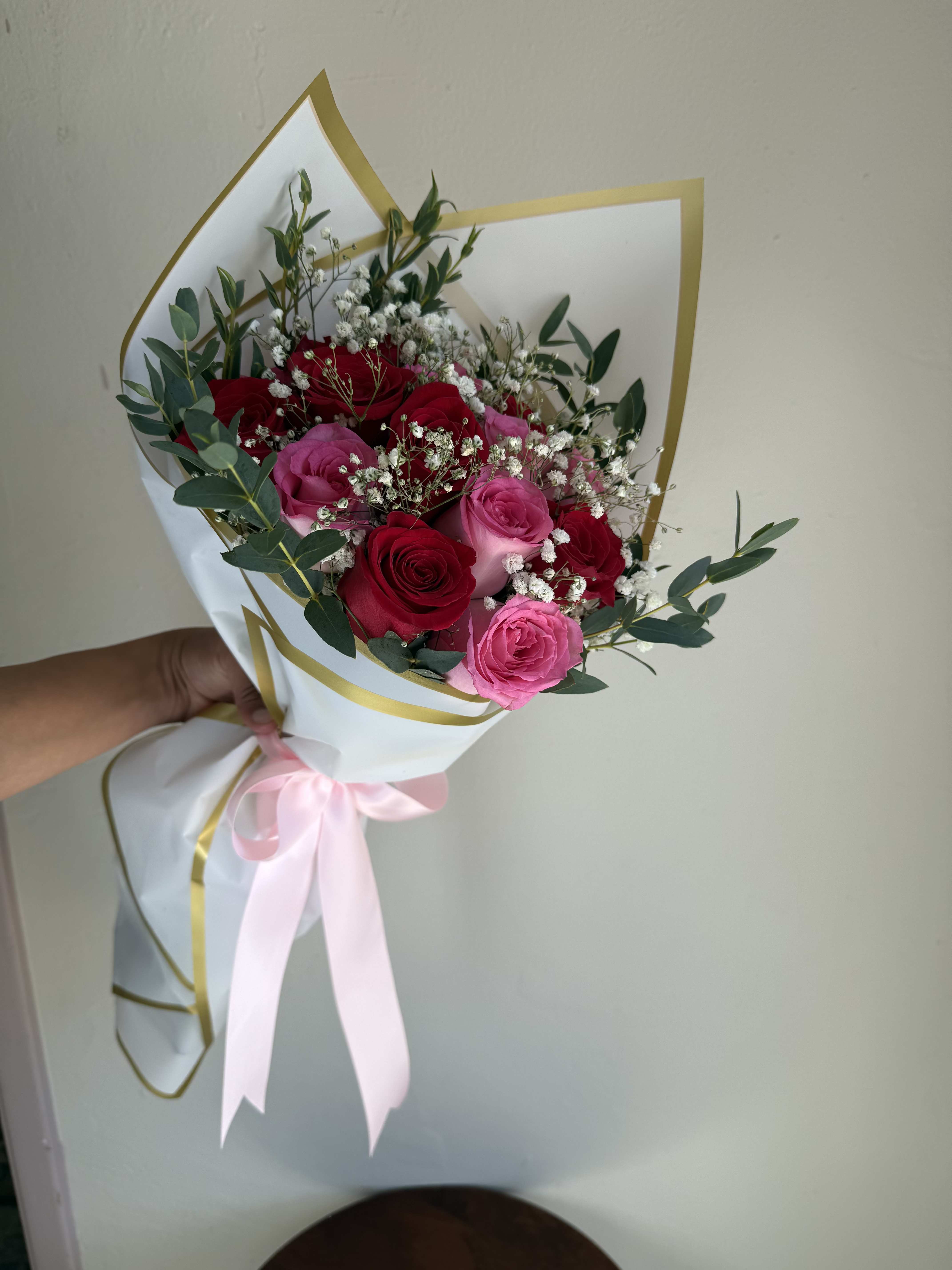 Bouquet of red and pink roses wrapped in white paper with a pink ribbon