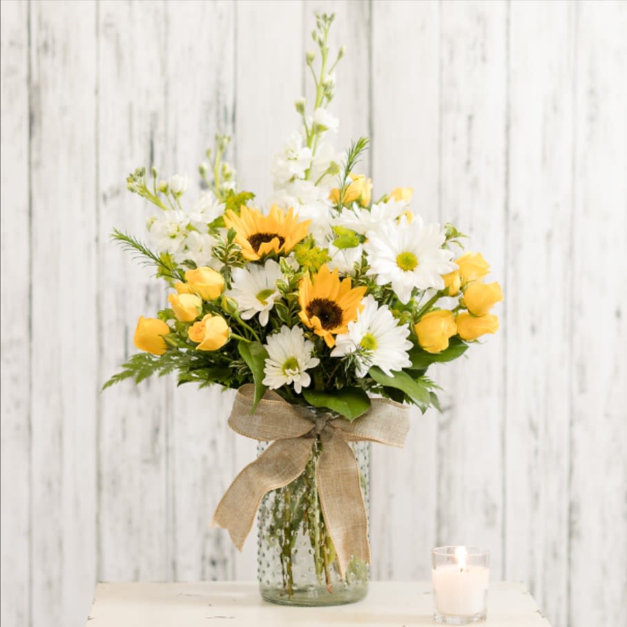 Yellow roses and white daisies in a glass vase with a burlap bow.