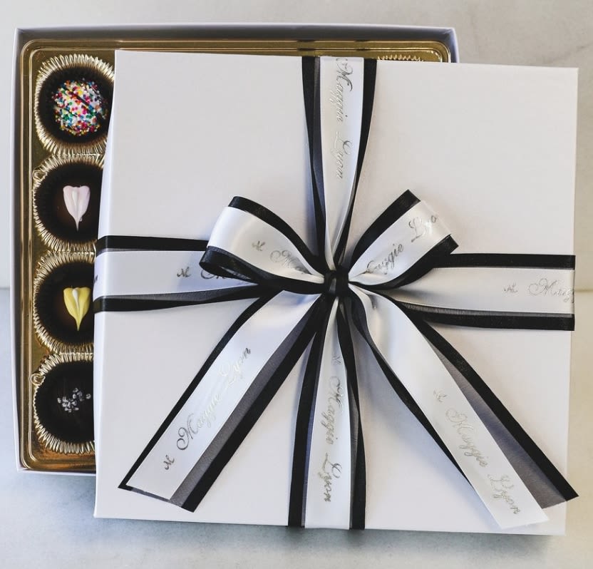 Gift box with black ribbon over a tray of assorted chocolates
