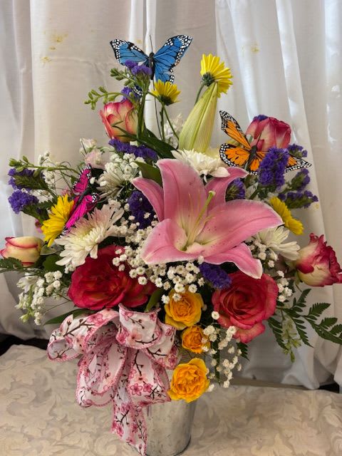 Minh's Garden - A minature garden is blooming with vibrant colors and whimsical butterflies.  Arranged in a tin vase a beautiful bright lily keeps spray roses, daisies, roses, babys breath and seasonal greenry in order. 