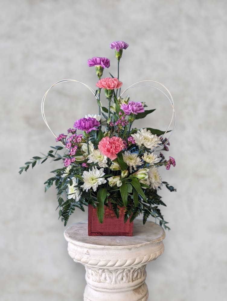 Mixed pink, purple, and white flowers in a red square container with heart loops