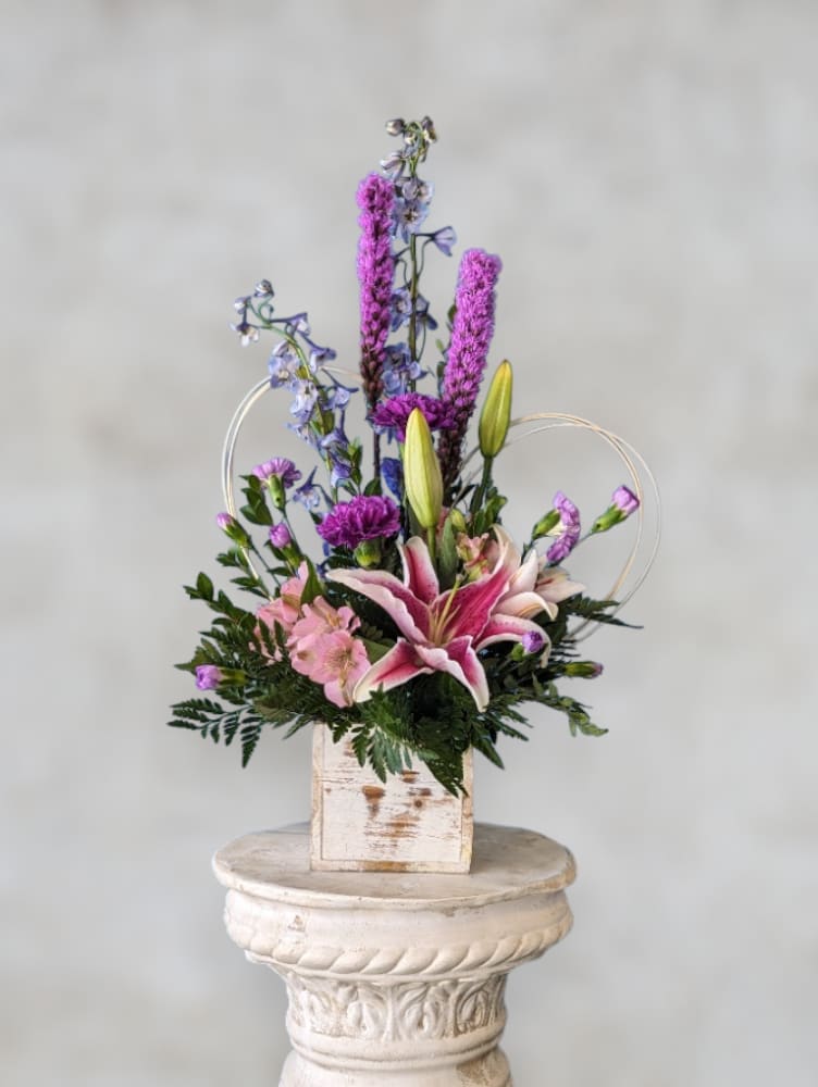 Pink lily arrangement with purple and blue flowers in a rustic wooden box