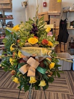 Large standing floral spray with yellow roses and greenery on a ribboned easel.
