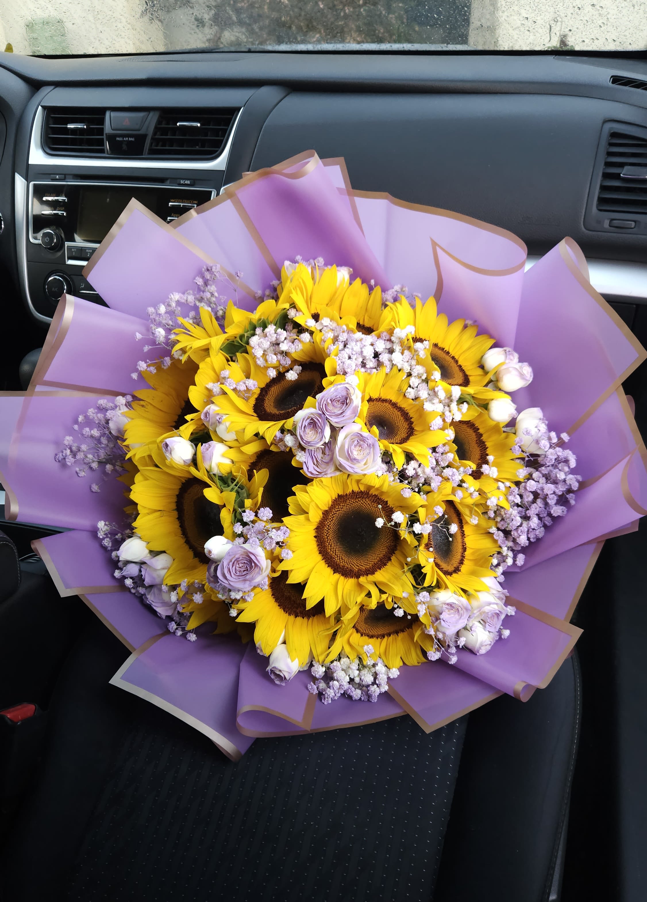 Ramo Buchón de Girasoles y Rosas (Amanecer Dorado &amp; Lavanda) - ​¿Buscas el regalo perfecto? Nuestro Ramo Buchón de Girasoles es la combinación ideal de frescura y diseño exclusivo. Este arreglo floral destaca por sus girasoles grandes y brillantes, acompañados de delicadas rosas color lila y una envoltura en papel coreano premium que eleva el estándar de cualquier celebración. ​ Características Principales: ​Flores Frescas: Girasoles de exportación y rosas seleccionadas.  ​Estilo Buchón: Diseño de gran formato con volumen y elegancia. ​ Ocasiones: Ideal para regalos de cumpleaños, aniversarios, graduaciones o simplemente para sorprender. ​ Envío de Flores en Miami: Servicio garantizado en Hialeah, Coral Gables y zonas aledañas. ​ ¿Por qué elegir este ramo de girasoles? A diferencia de un ramo común, este diseño integra texturas de baby's breath blanca y lila, creando un contraste visual que resalta en cualquier fotografía. Es el detalle perfecto para quienes buscan arreglos florales modernos y lujosos.