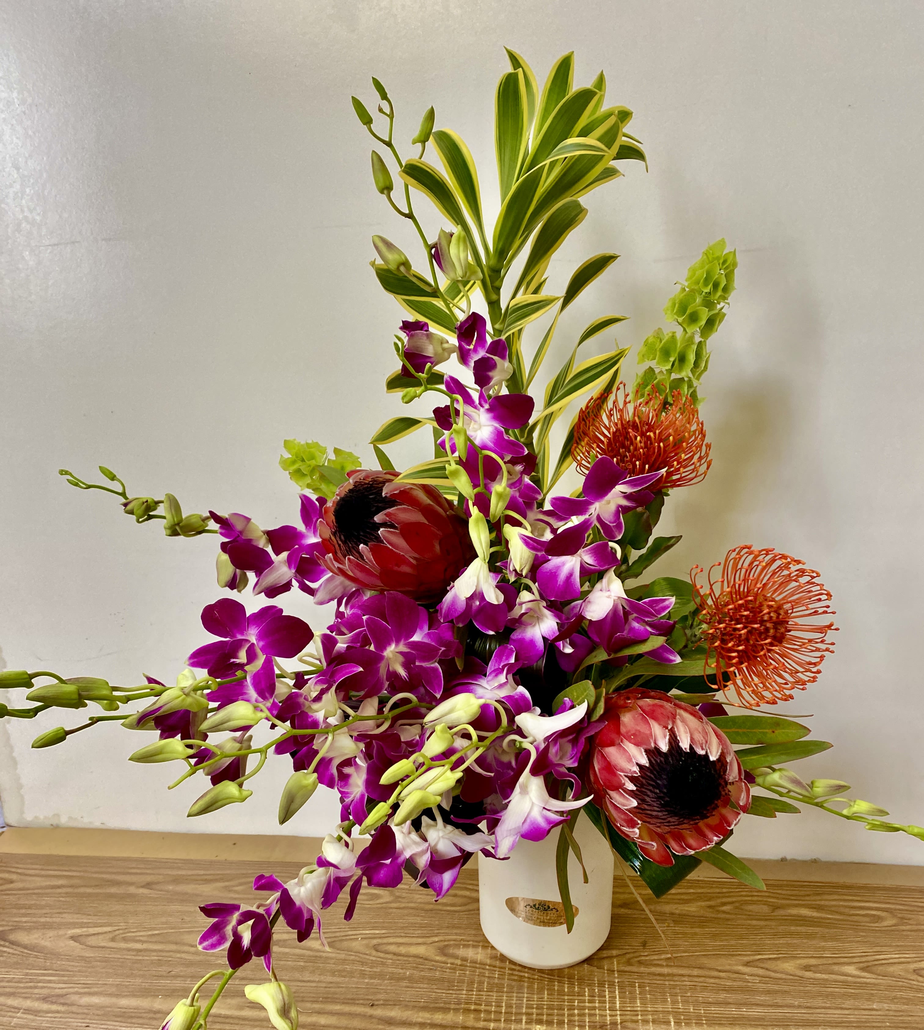 Tropical floral arrangement with purple orchids and red protea in a white vase