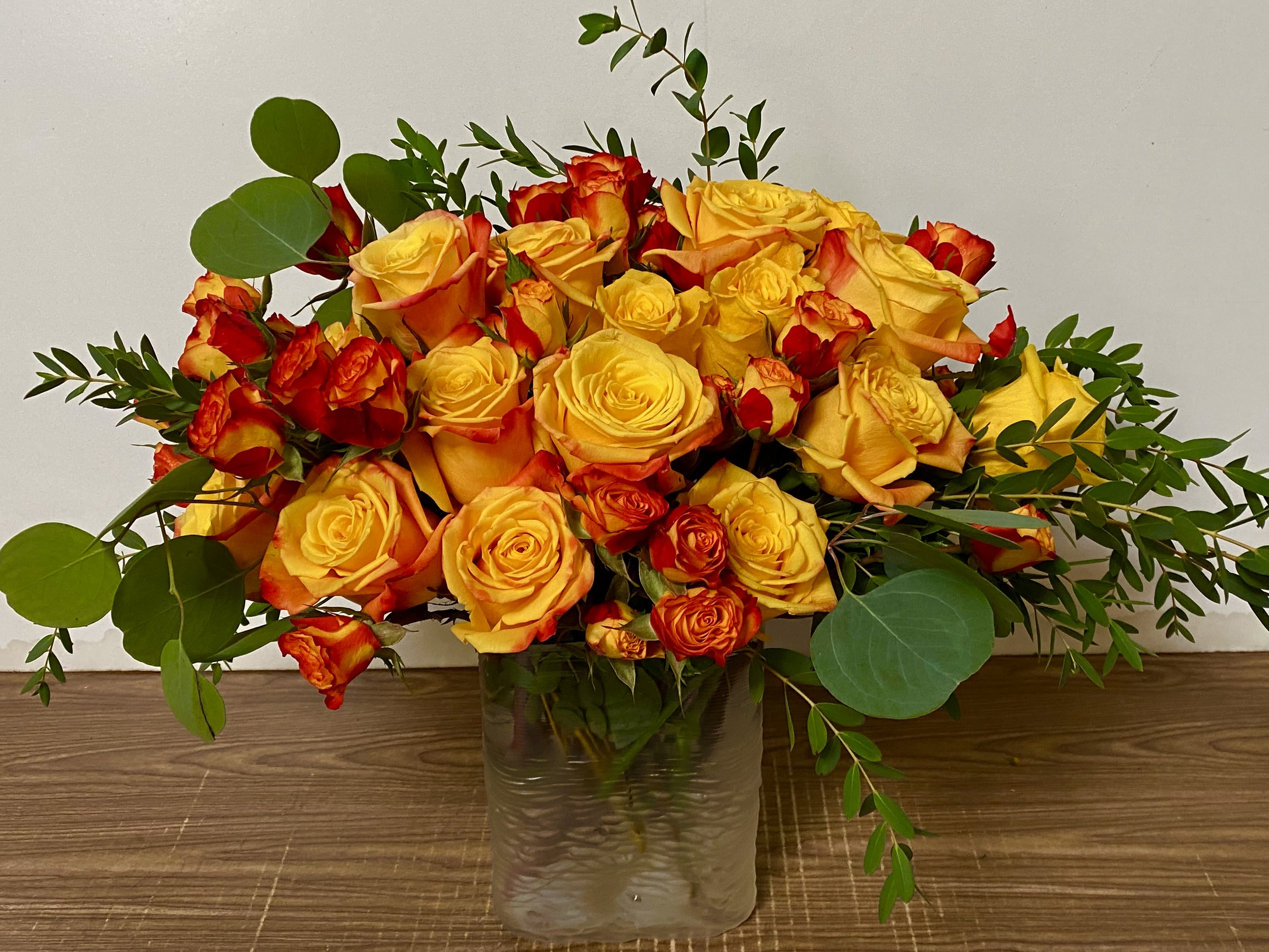 Yellow and orange roses arranged in a clear glass vase