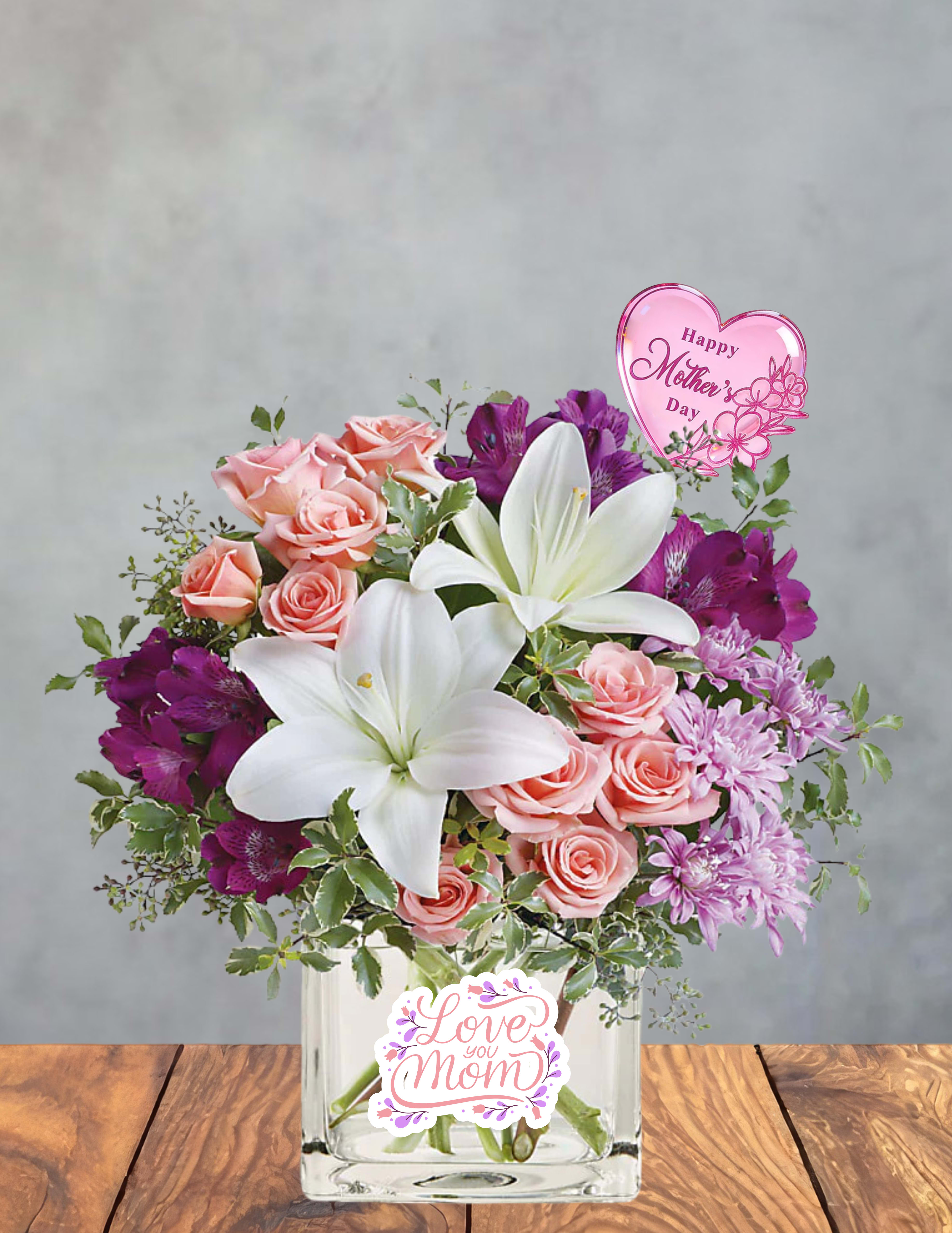 Petals of Gratitude - Petals of Gratitude   A soft, heartfelt expression of appreciation, this bouquet gathers lilies, blush roses, lavender blooms, and delicate accents of greenery into a soothing garden‑inspired embrace. Each stem is chosen for its quiet elegance, creating a design that feels both uplifting and tender. Finished with a sweet “Love You Mom” touch, it’s a graceful way to honor her presence, her care, and the love she’s poured into every season of your life.