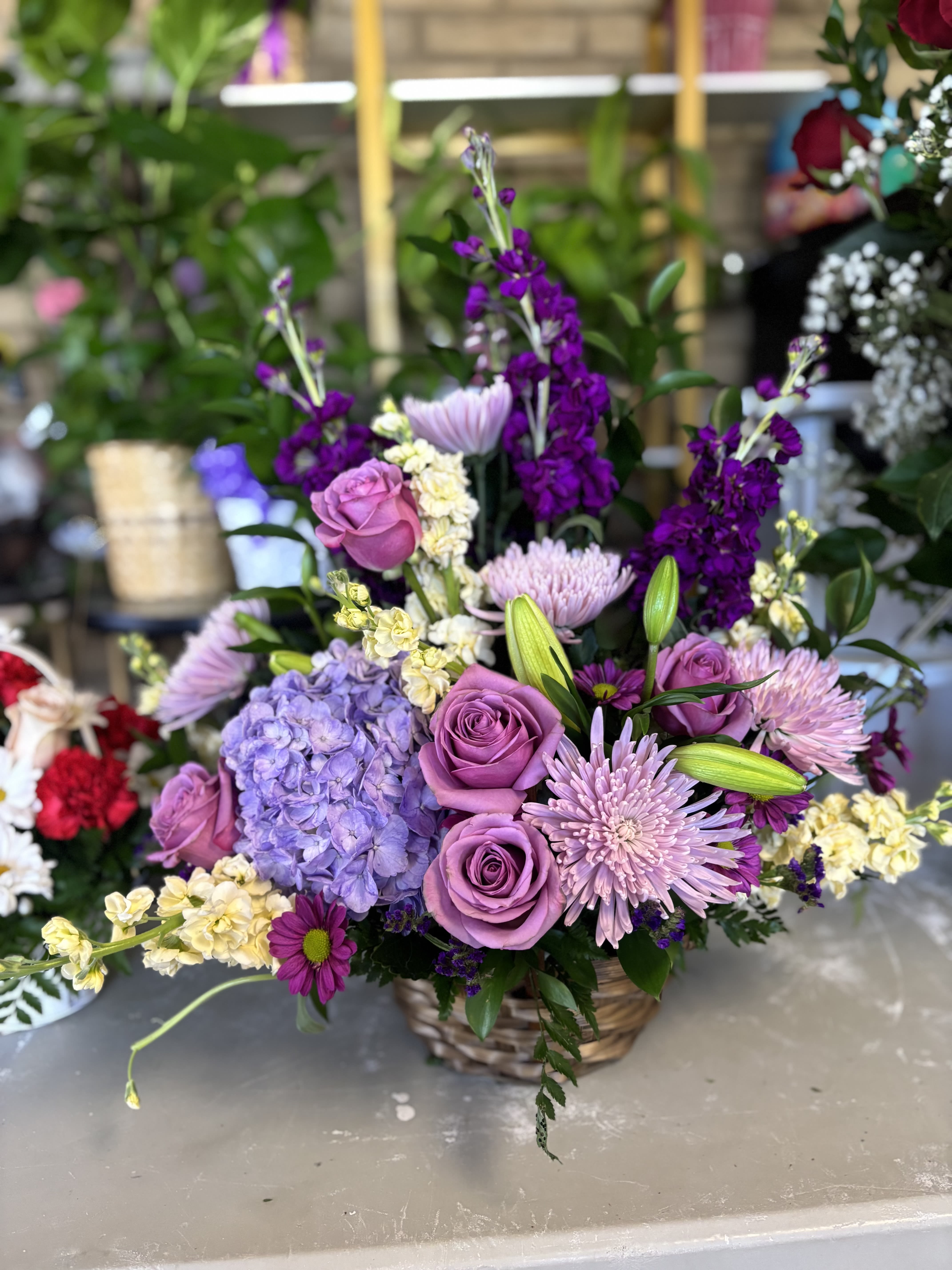 Lavender roses and purple flowers arranged in a wicker basket