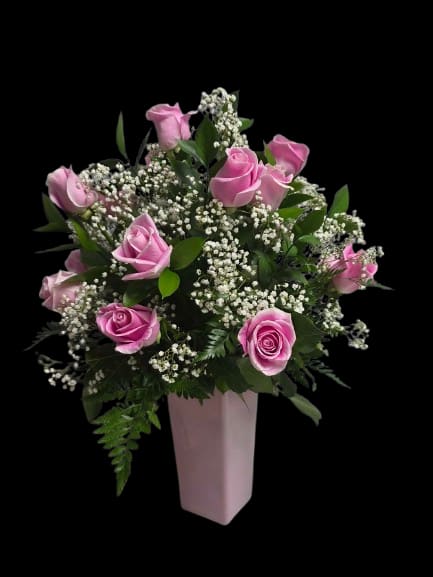 classic pink - Soft pink roses clustered with airy white filler create a romantic birthday bouquet or Mother's Day arrangement that feels both gentle and polished. This flower arrangement for anniversaries or everyday gifting places the blooms in a tall, tapered pink vase, giving the display an upright, formal presence that will make the person you're thinking of feel truly celebrated.  The composition is full and rounded at the top, with deep green foliage framing the soft pink roses and tiny white accents for contrast and texture. The arrangement arrives in a pink vase that complements the rose tones and adds immediate shelf-ready polish; its height makes it a striking centerpiece for a dining table or entry console. Ideal for saying "thinking of you," "happy birthday," or "thank you," this bouquet is an easy, elegant way to brighten someone's day.