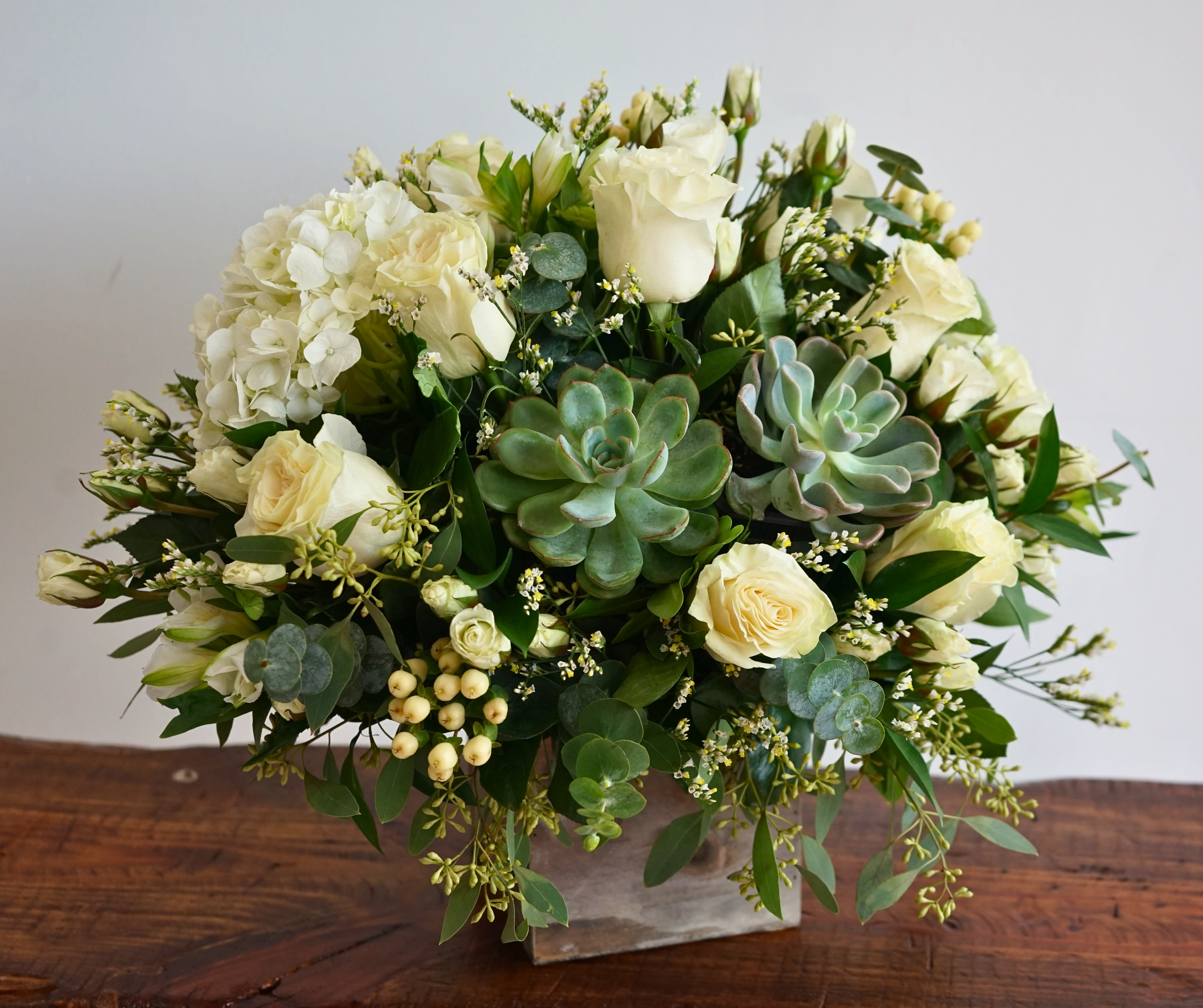 Whimsical Wonders - Flowers can inspire feelings of pure happiness, both with their beauty and the sentiment behind them. Our charming, country-inspired bouquet delivers that joy with soothing, pearl-white blooms in a loose, natural style and a fresh succulent for an extra eye-catching touch. Complementing the arrangement is our grey-washed wooden cube, with soft tones and natural textures that add warmth to any décor. All-around arrangement with white roses, hydrangeas, cream hypericum and eucalyptus; accented with pre-picked succulents, silver dollar eucalyptus and assorted greenery Artistically designed in our exclusive grey washed wooden cube with rustic style.
